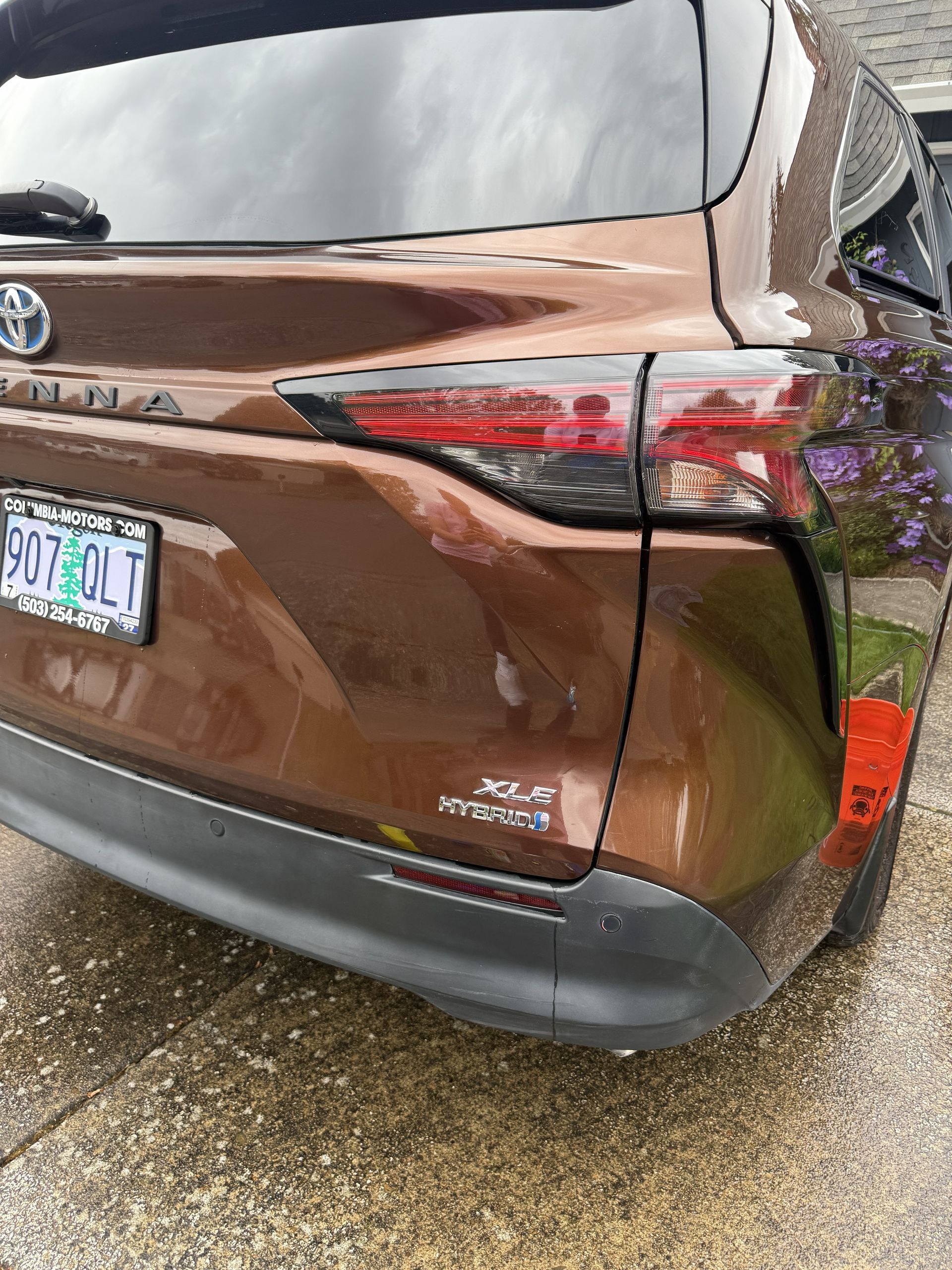 Rear view of a brown Toyota SUV with a visible taillight and license plate on a wet driveway.