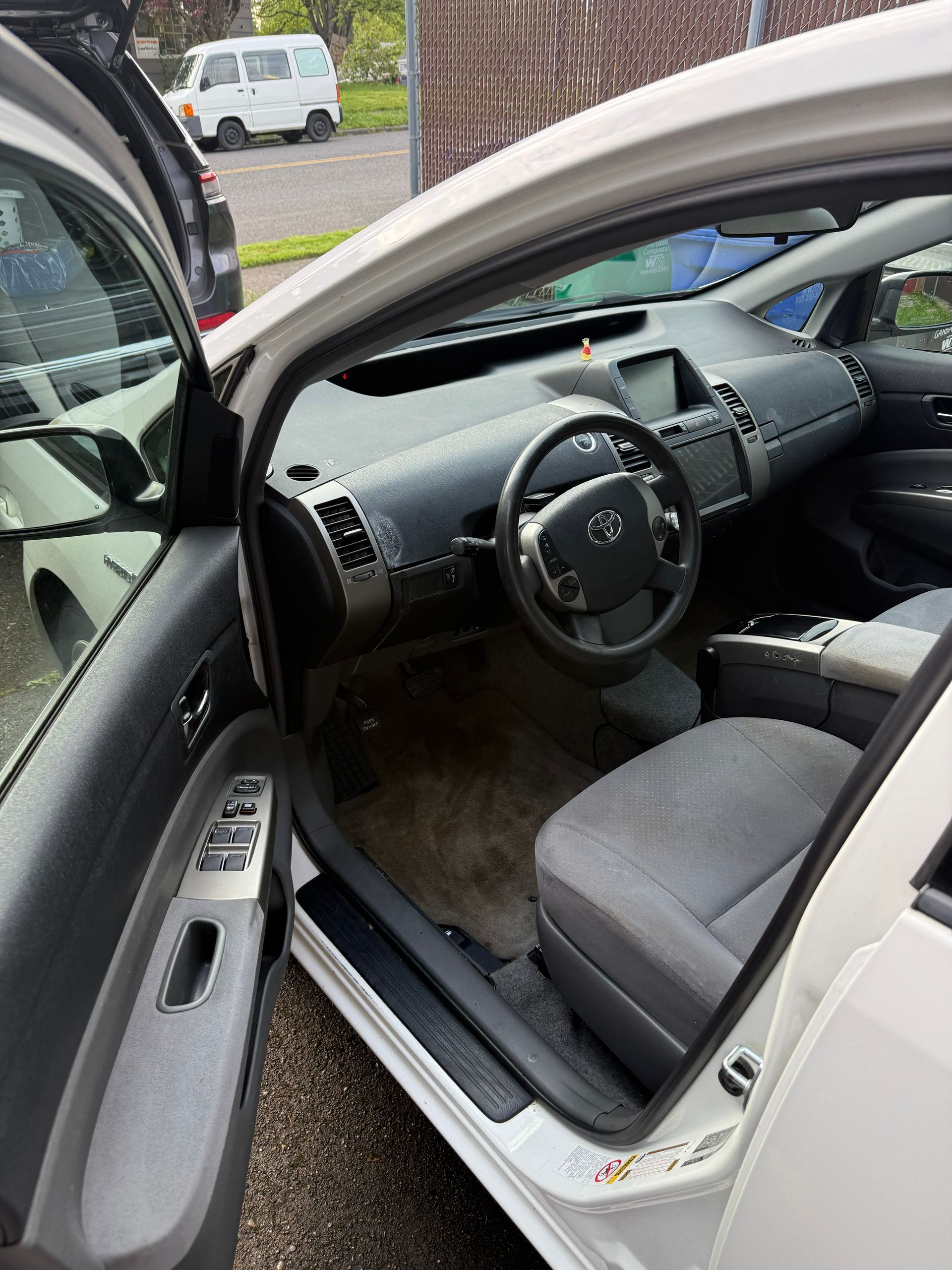 Open car door showing a beige interior, steering wheel, and front seat from outside on a driveway.