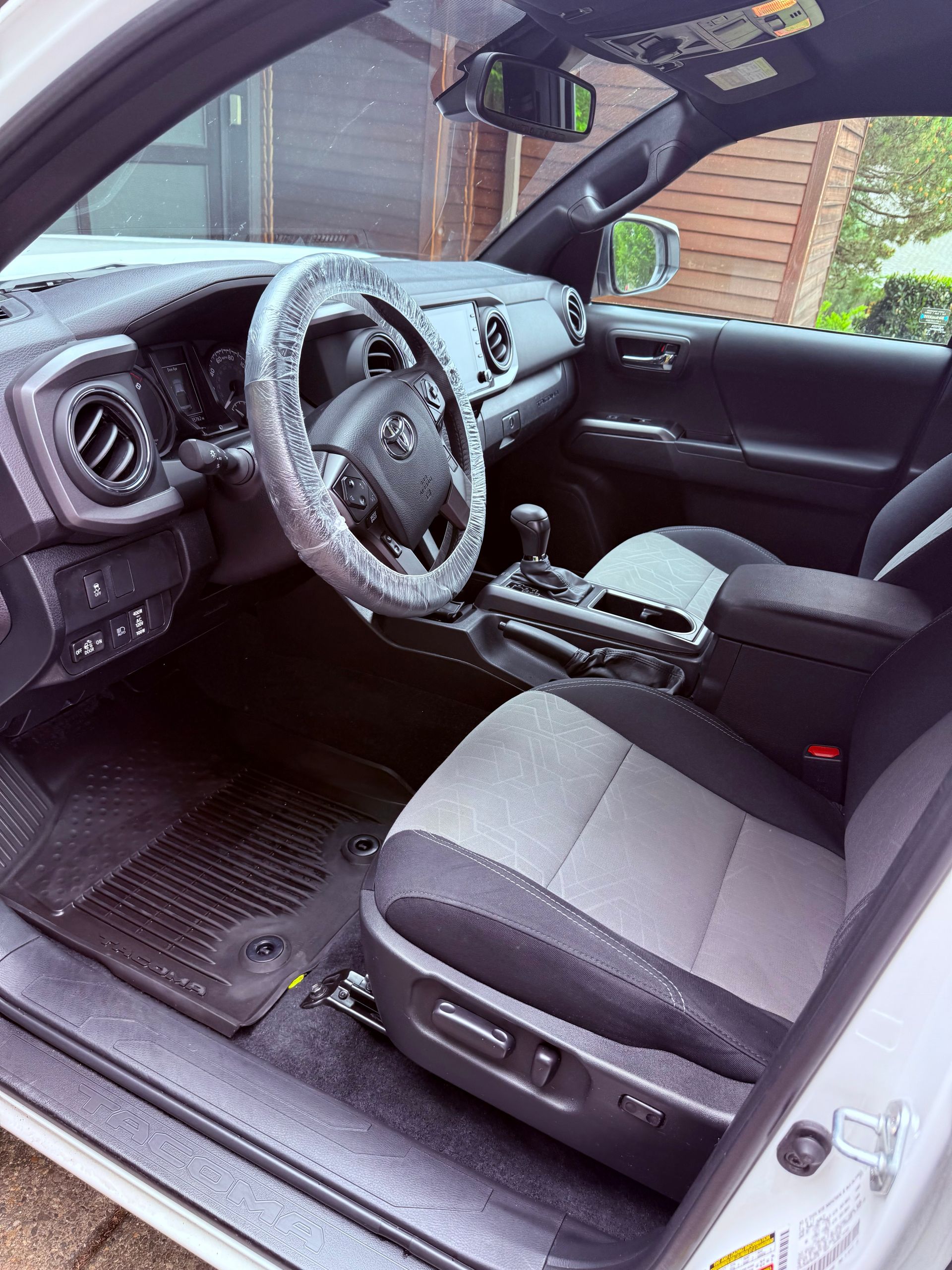 Car interior with black and gray seats, dashboard, steering wheel, and center console seen from the open door