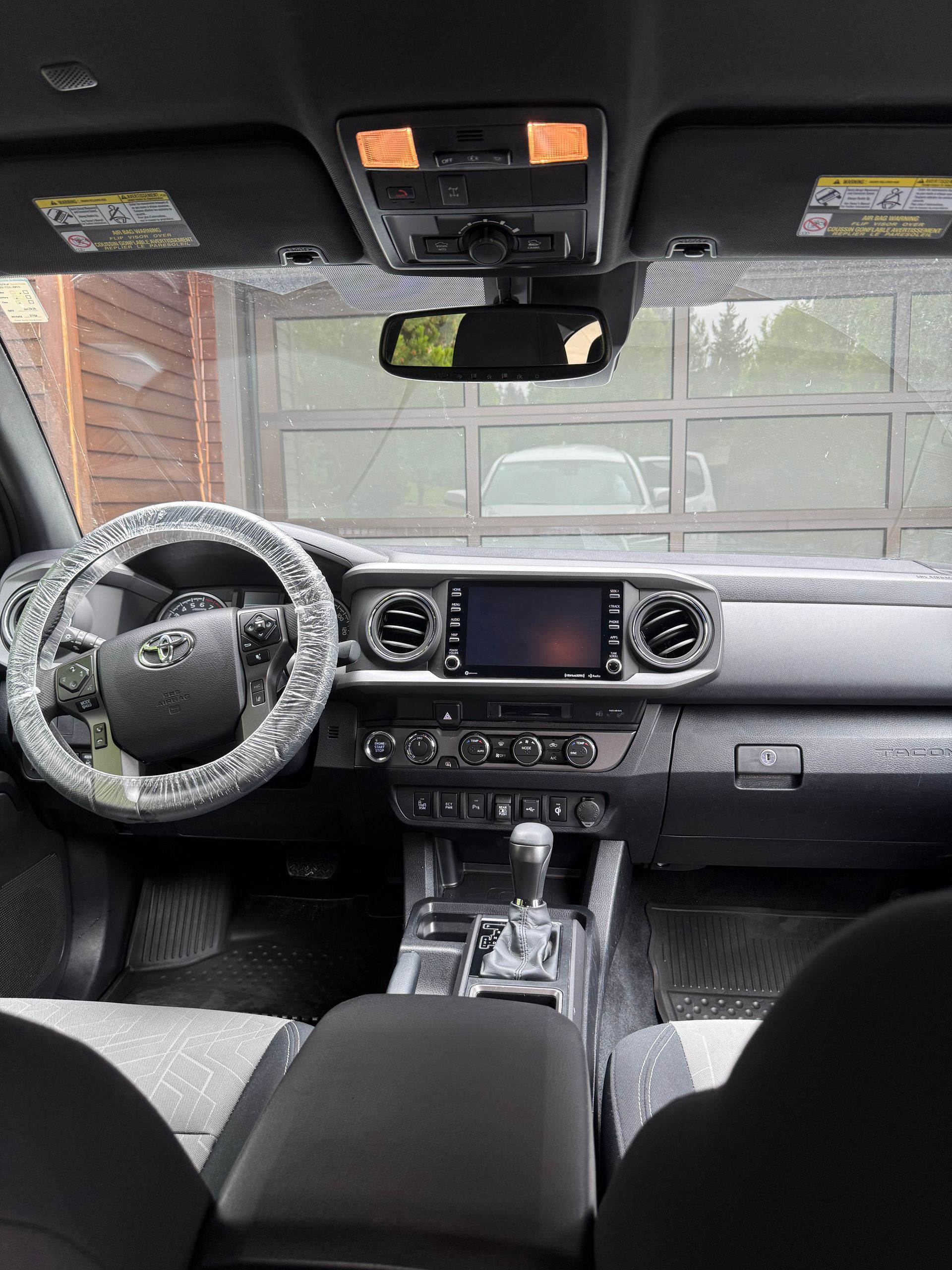 Interior of a black car, showing the steering wheel, dashboard, center console, and garage reflected in the windshield.