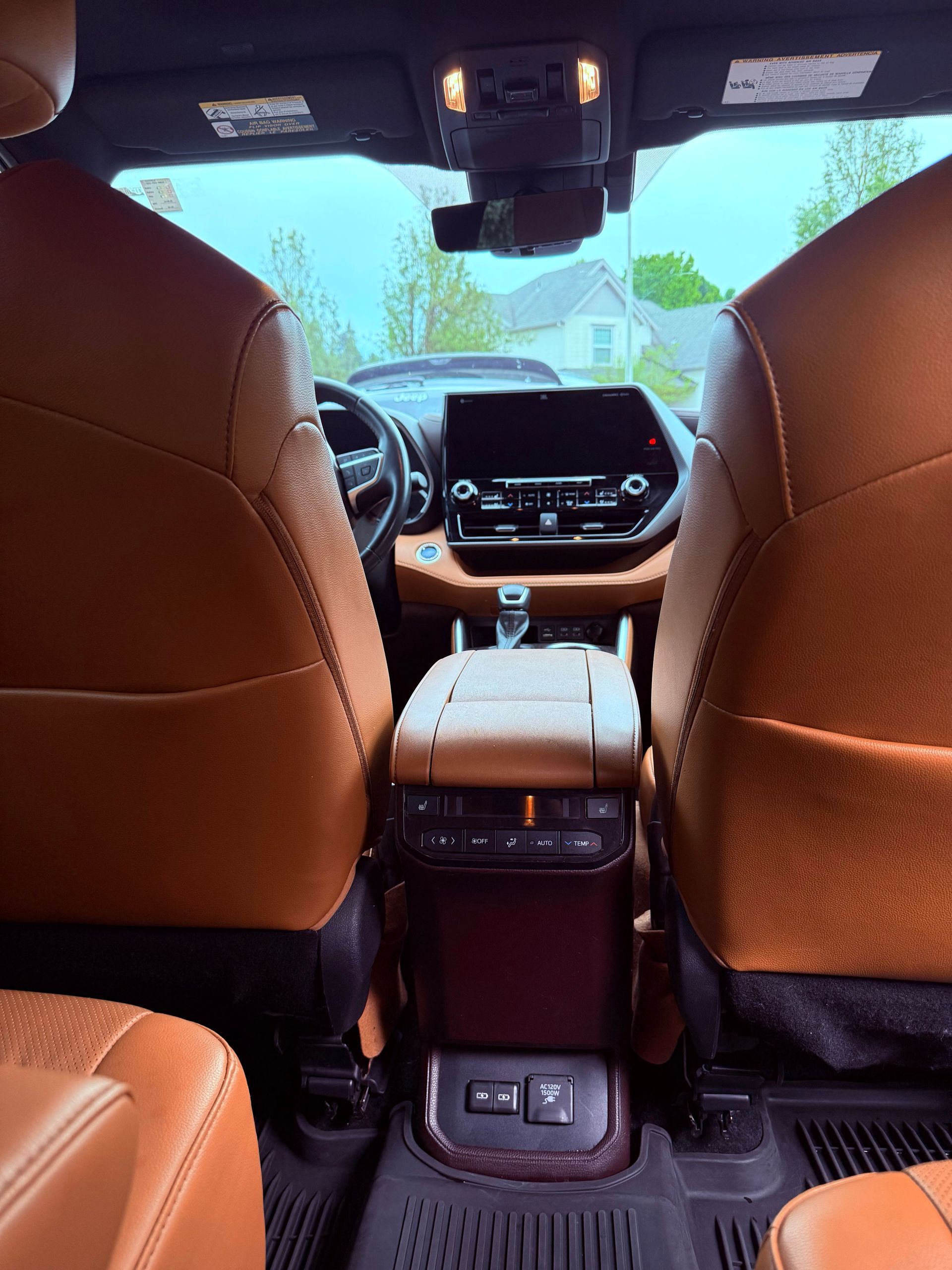 View from back seat of a tan car interior, looking past front seats toward the dashboard and windshield.