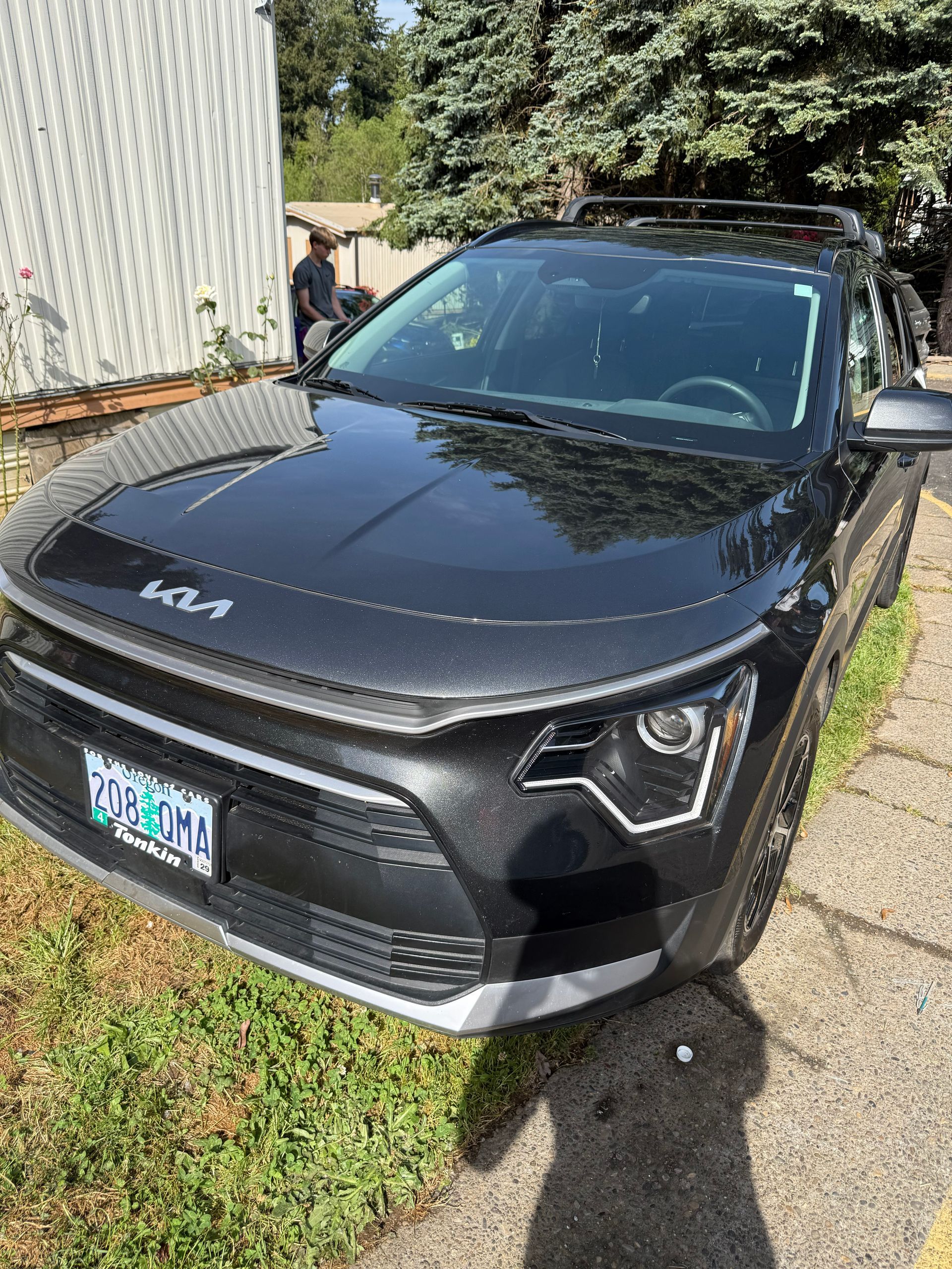 Black Kia SUV parked on grass beside a white building, front view in sunlight