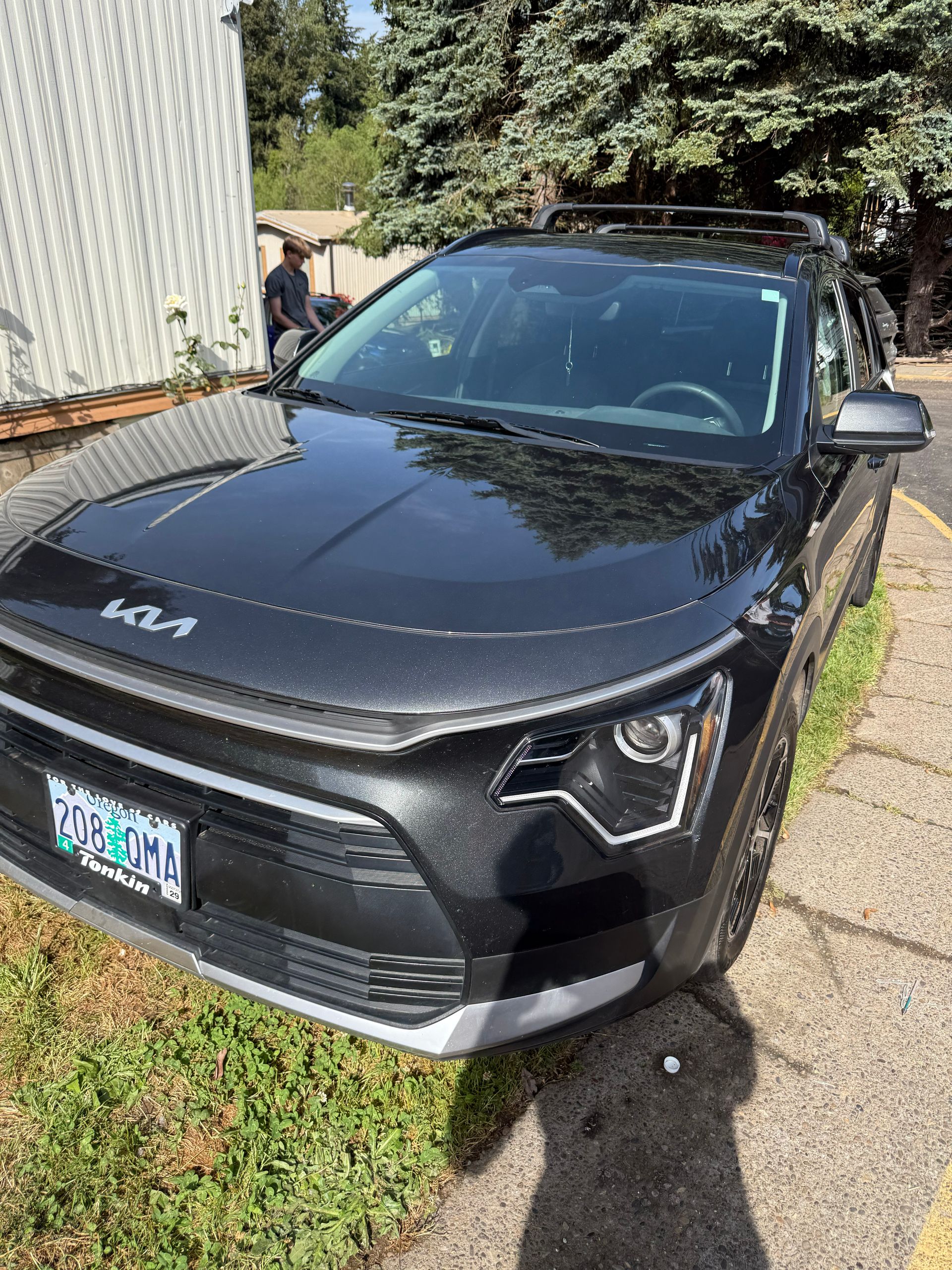 Black Kia SUV parked on grass beside a sidewalk and house, front view in sunlight