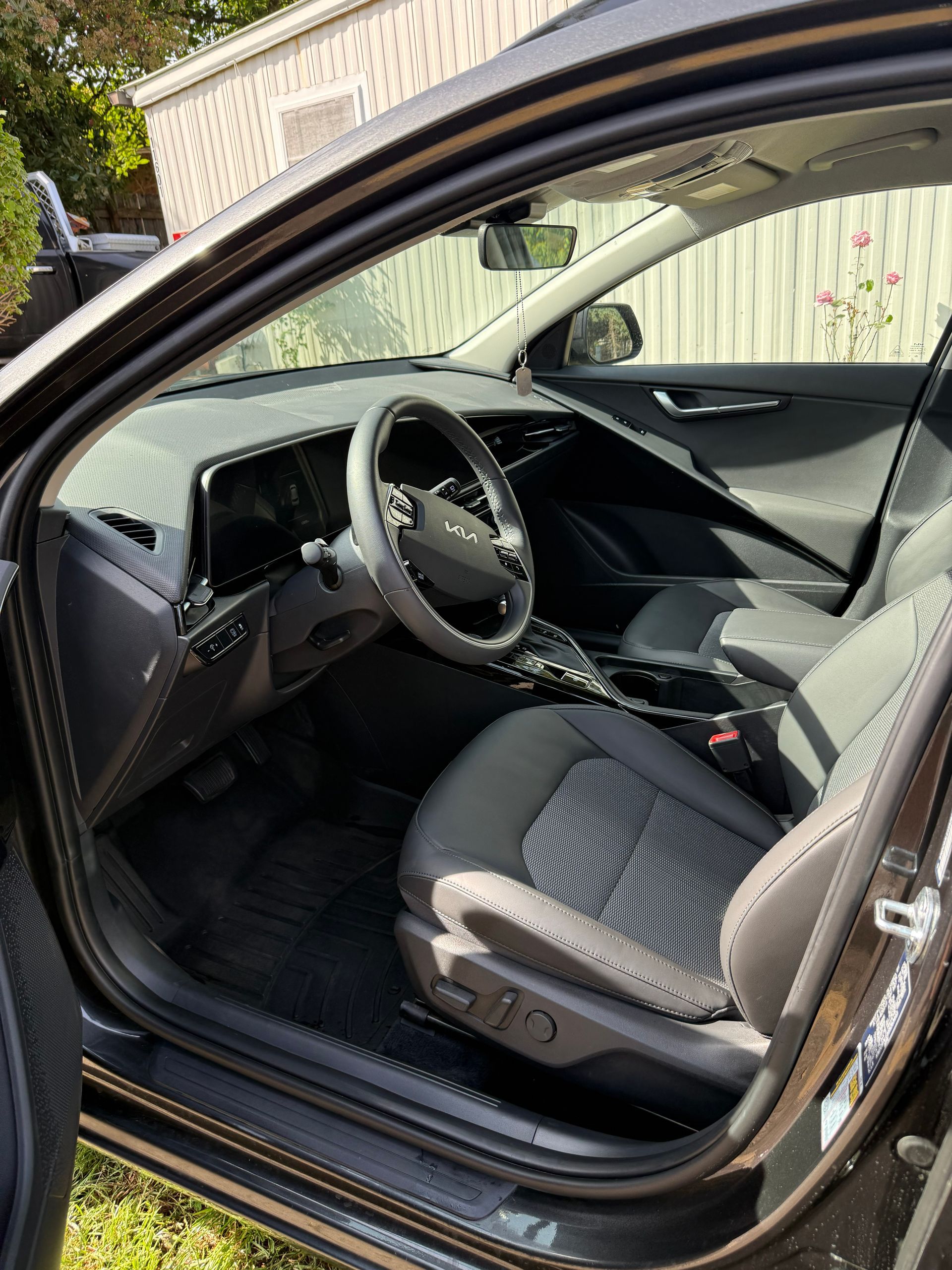 Open car door showing a black interior, driver’s seat, dashboard, and steering wheel in daylight.