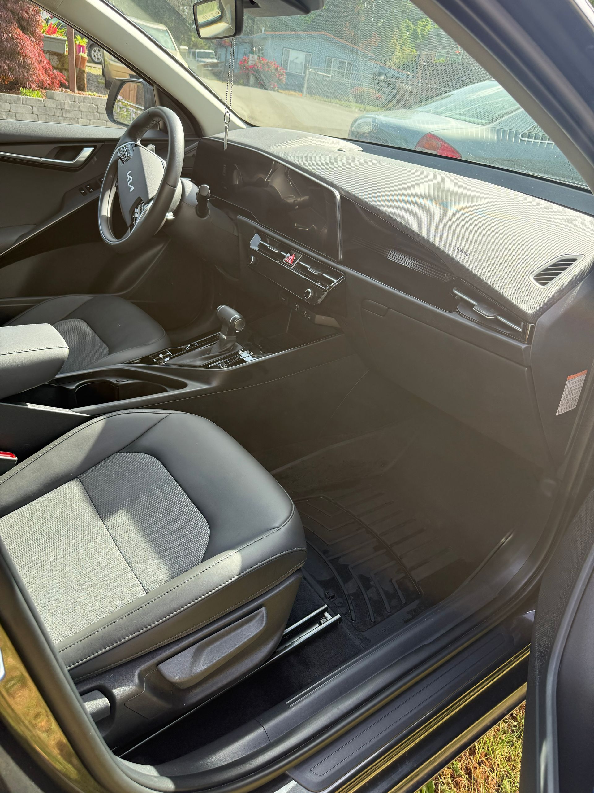 Car’s front interior with gray seats, open door, and dashboard in sunlight.