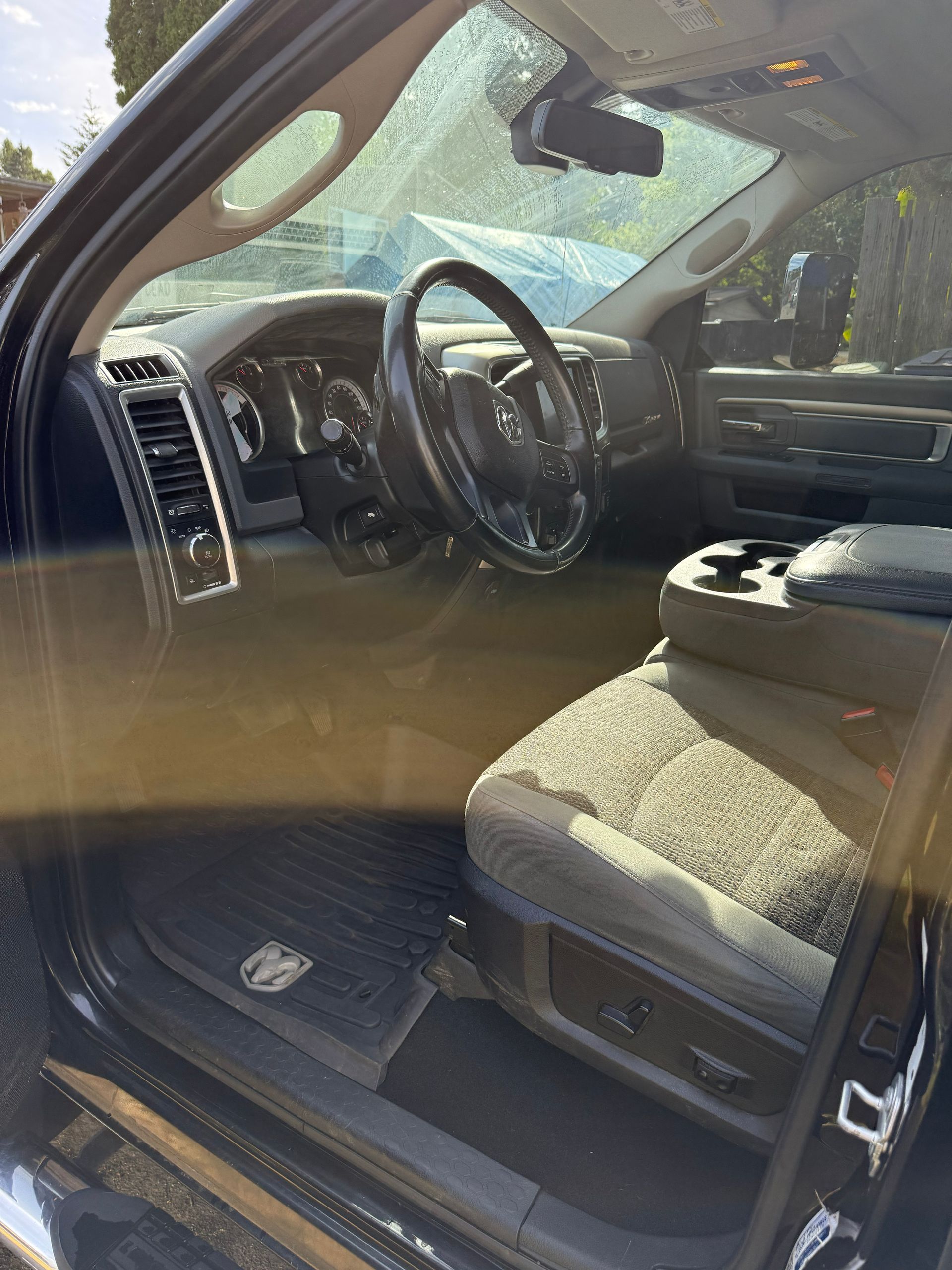 Open car door showing black steering wheel and gray cloth front seat in sunlight
