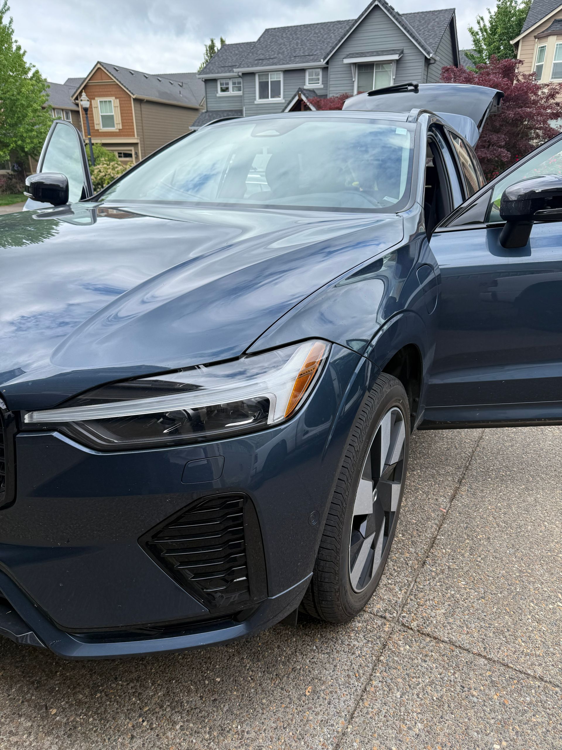 Dark blue SUV parked in a suburban driveway, front view, with a driver visible through the open door.