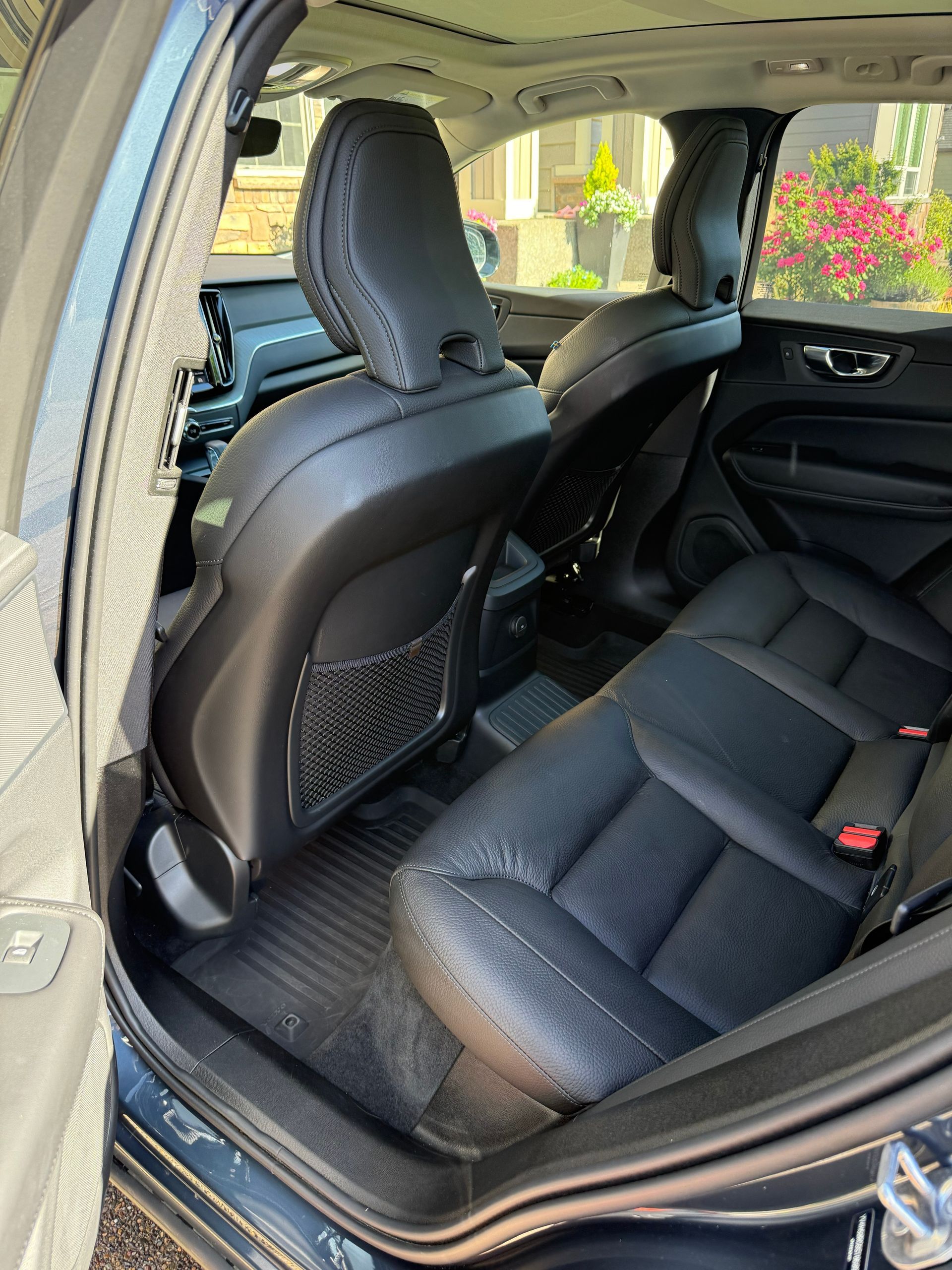 Open car rear door showing black leather back seat and front seat interior, with sunlight outside.