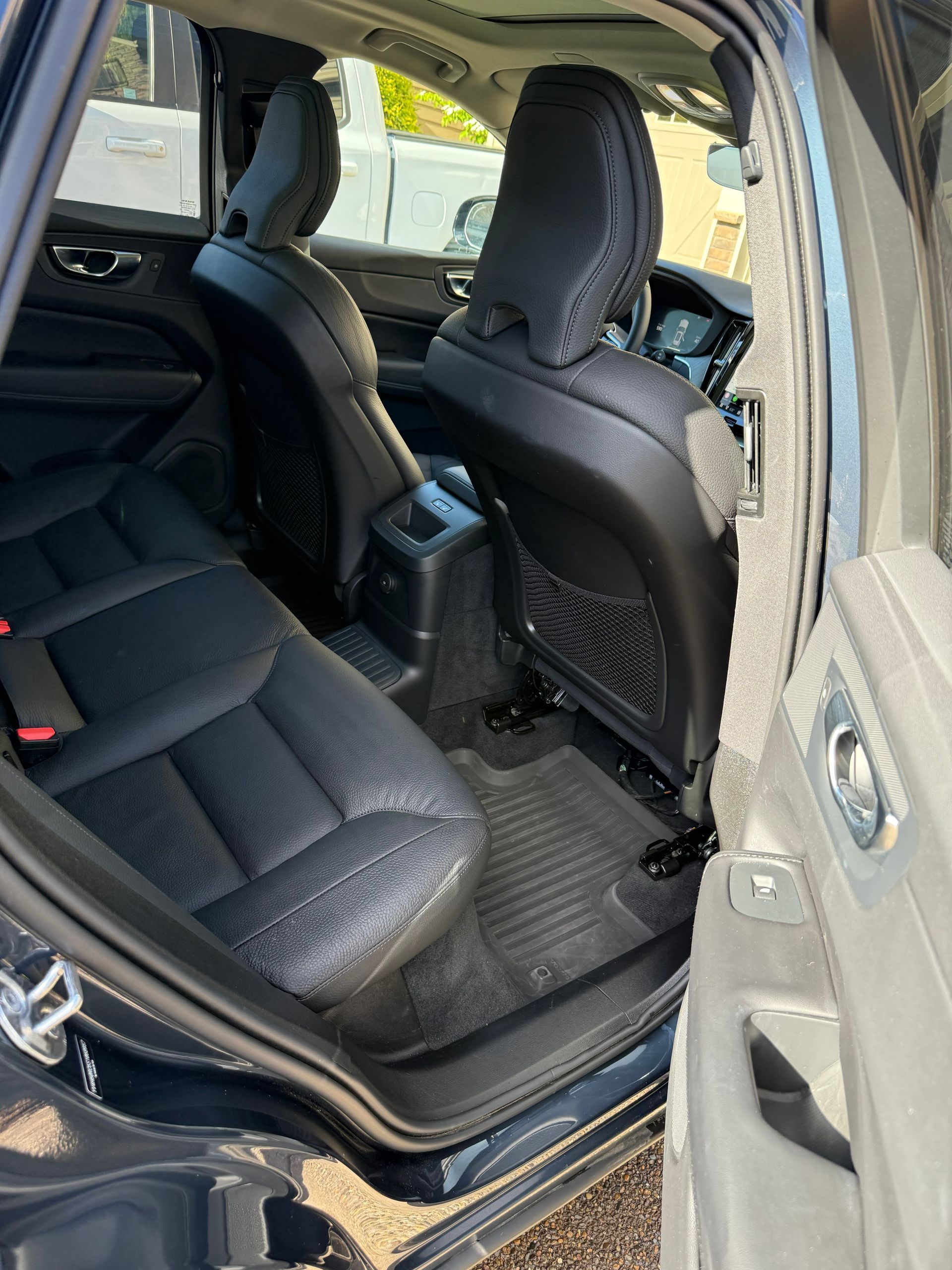 Rear car interior with black leather seats and open door, showing the back seat and front passenger seat