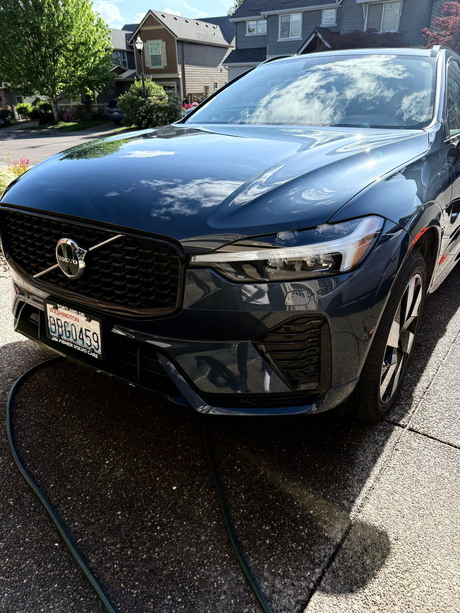 Black Volvo sedan parked in a driveway, wet from washing, with a suburban house in the background