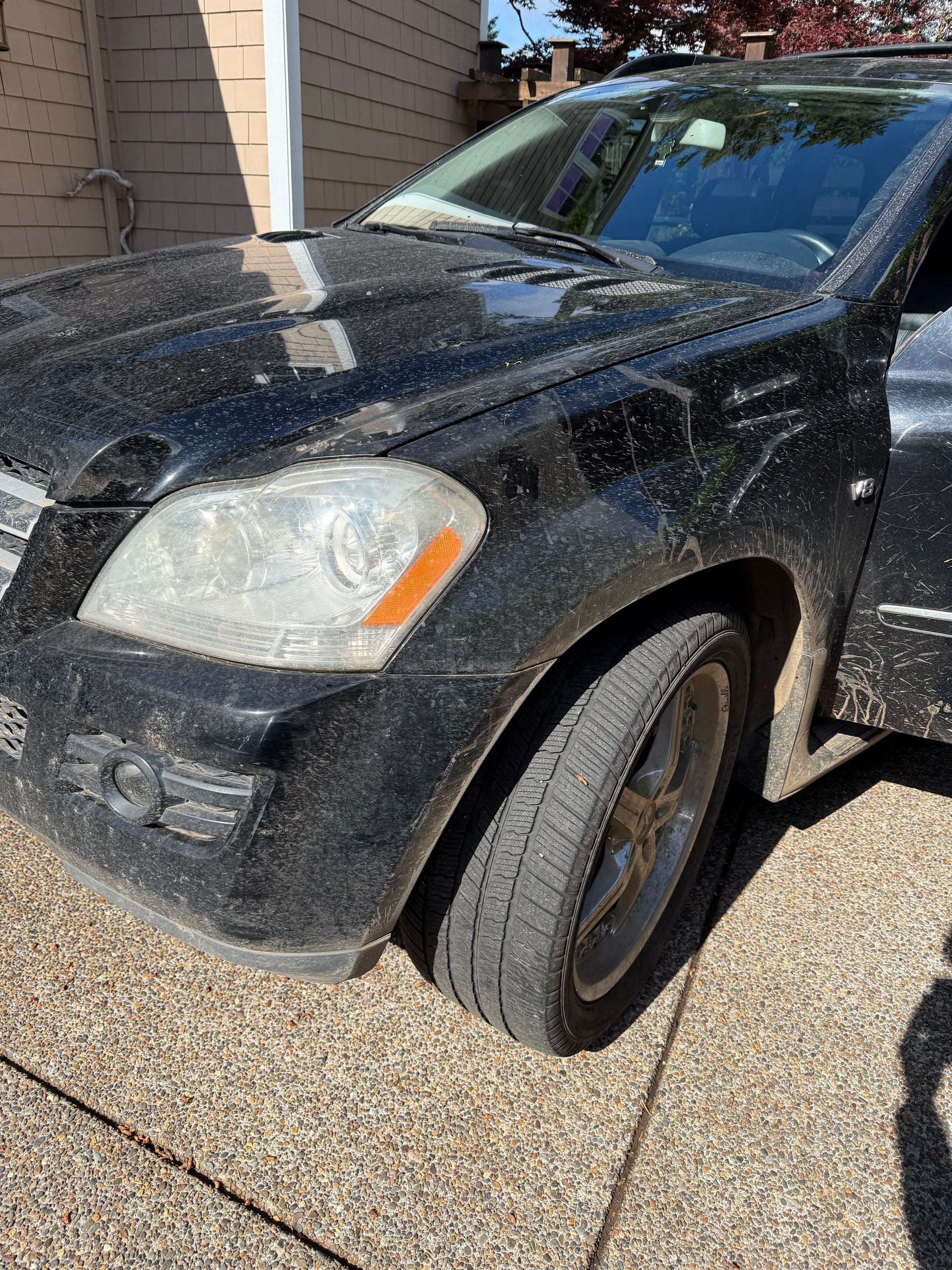 Black car parked beside a building, front passenger side damaged and scraped.
