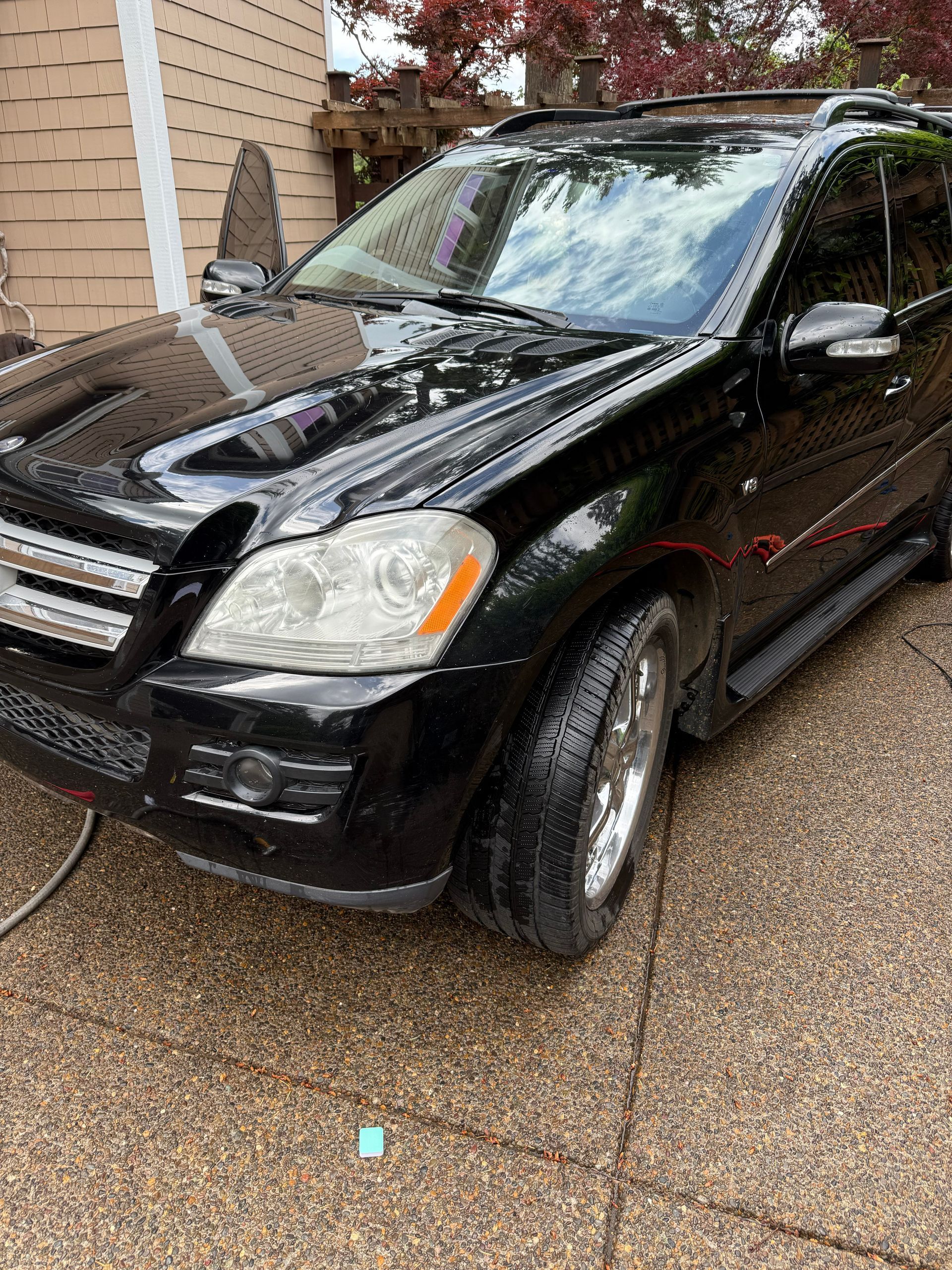 Black SUV parked in a driveway beside a house, with a wet driveway and reflections on the hood