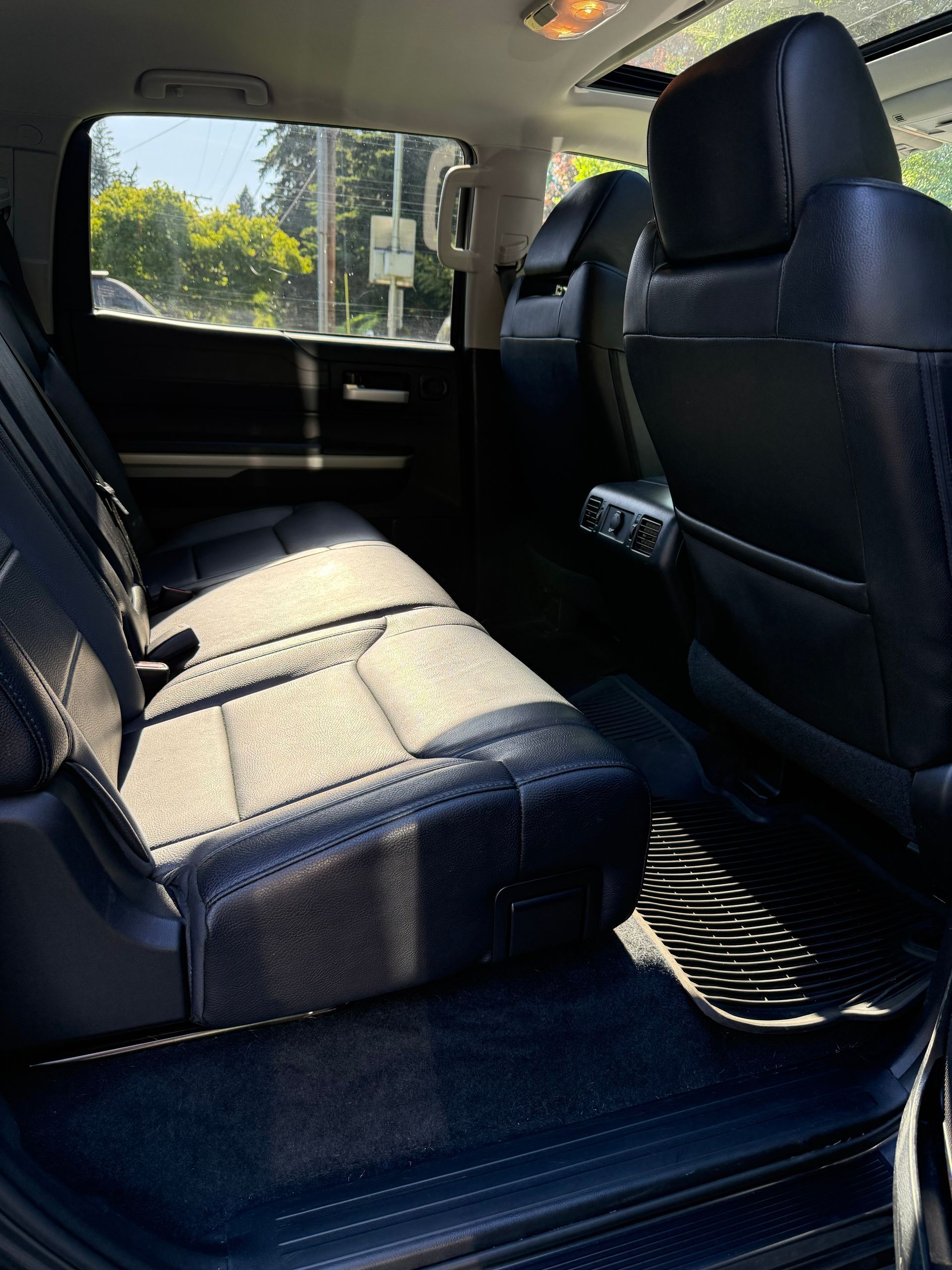 Car interior with black leather seats and a rear bench, viewed from the open side door.