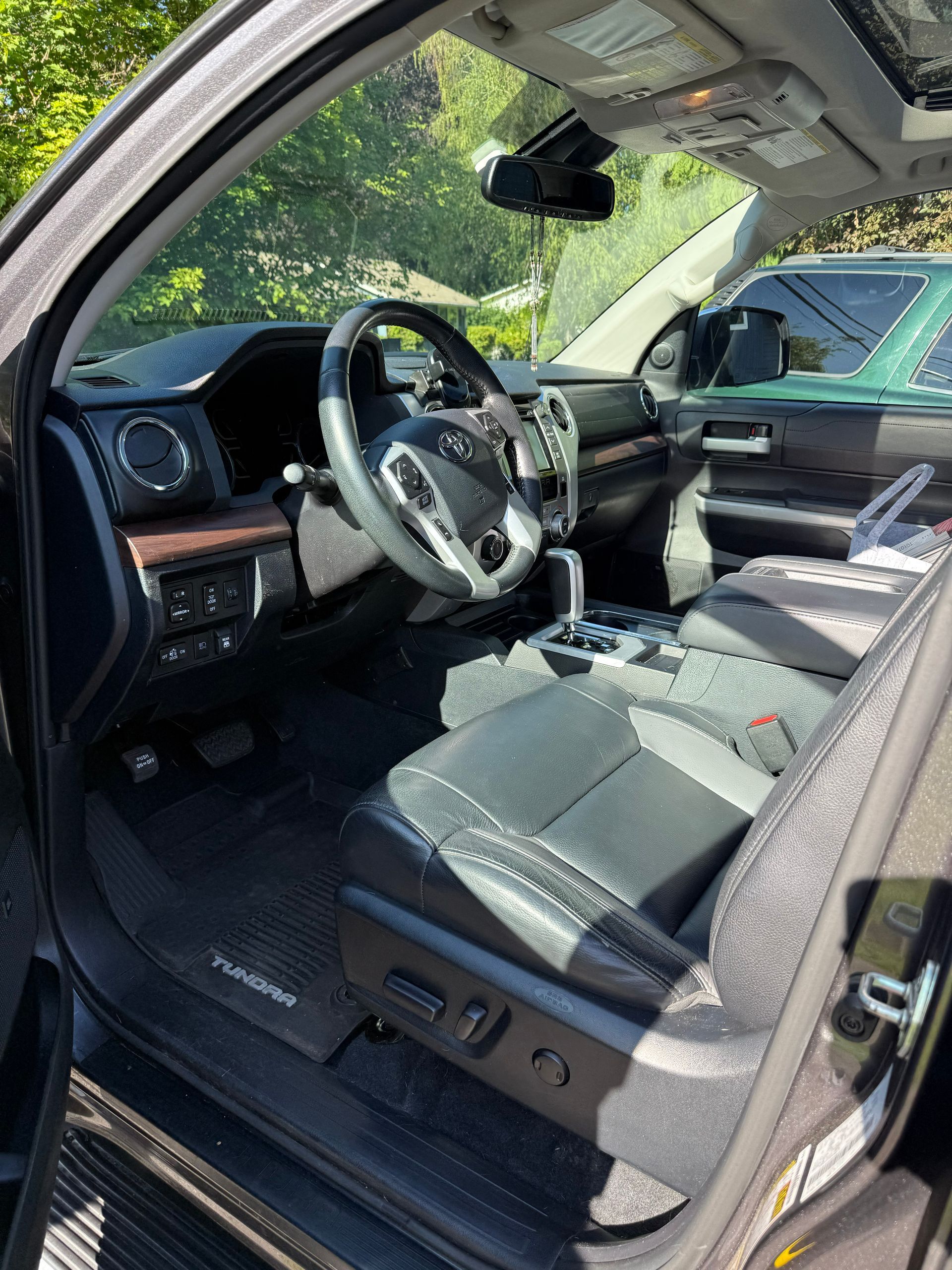 Car interior with black leather seats and steering wheel, viewed through the open driver’s door.