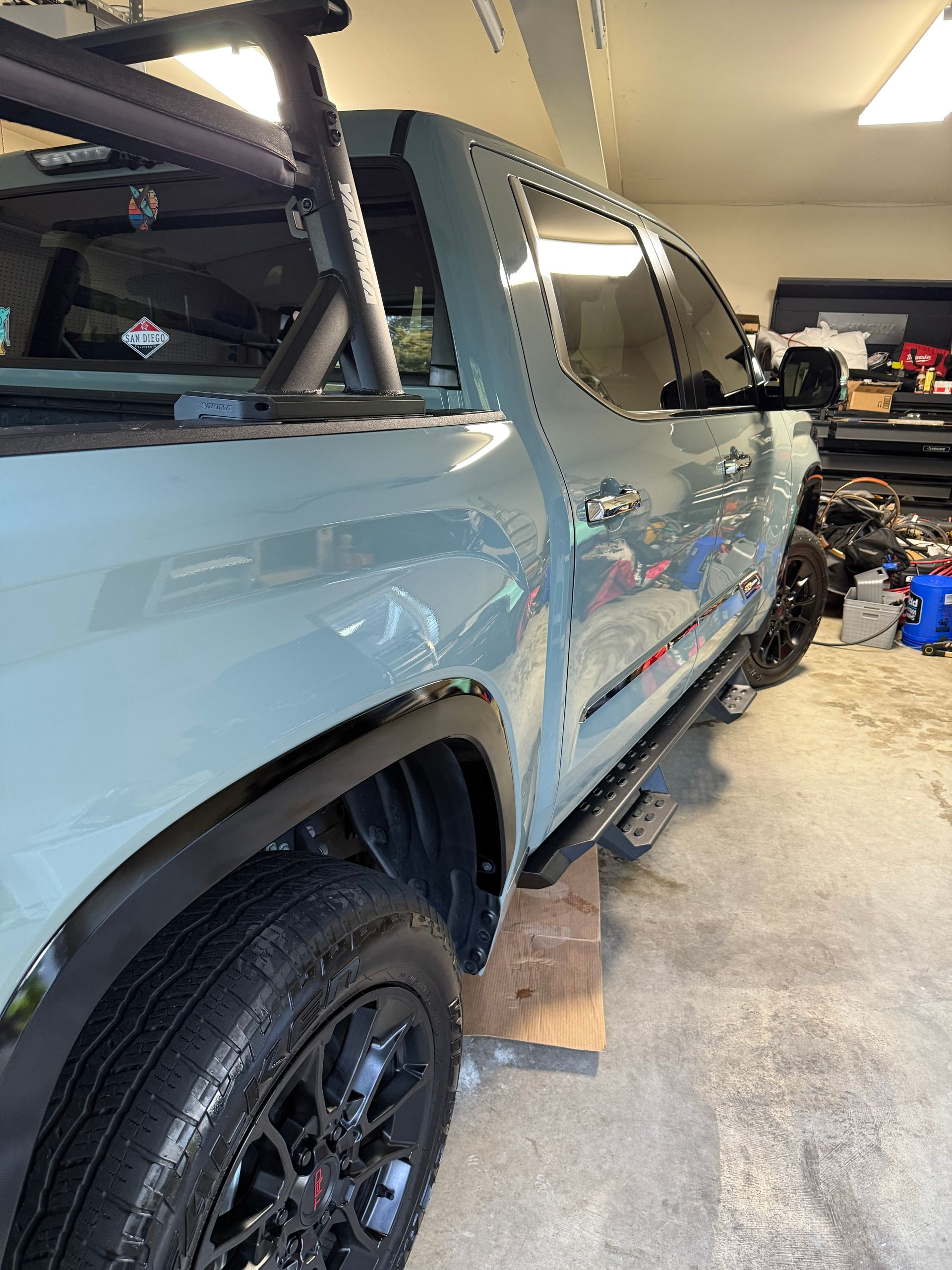 Blue pickup truck parked in a garage, side view with black wheels and running boards.