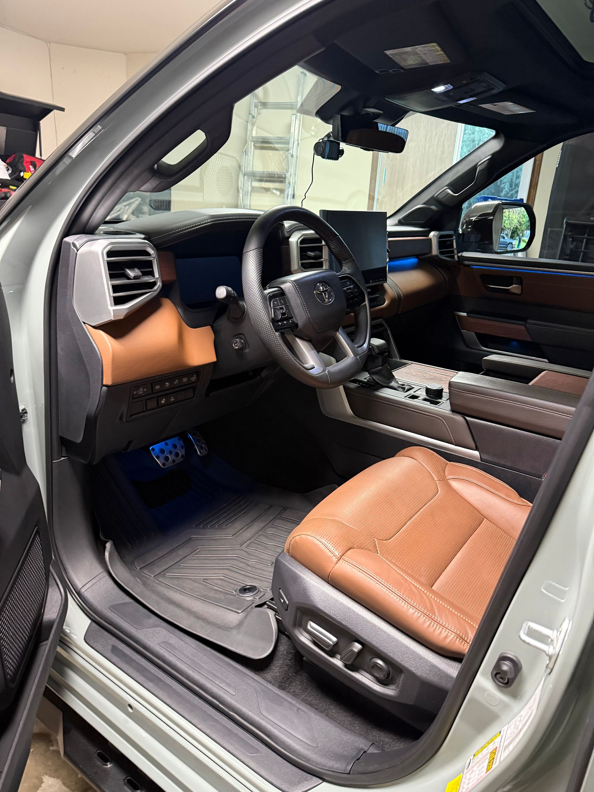 Car interior with tan leather seats, black dashboard, and driver-side door open.