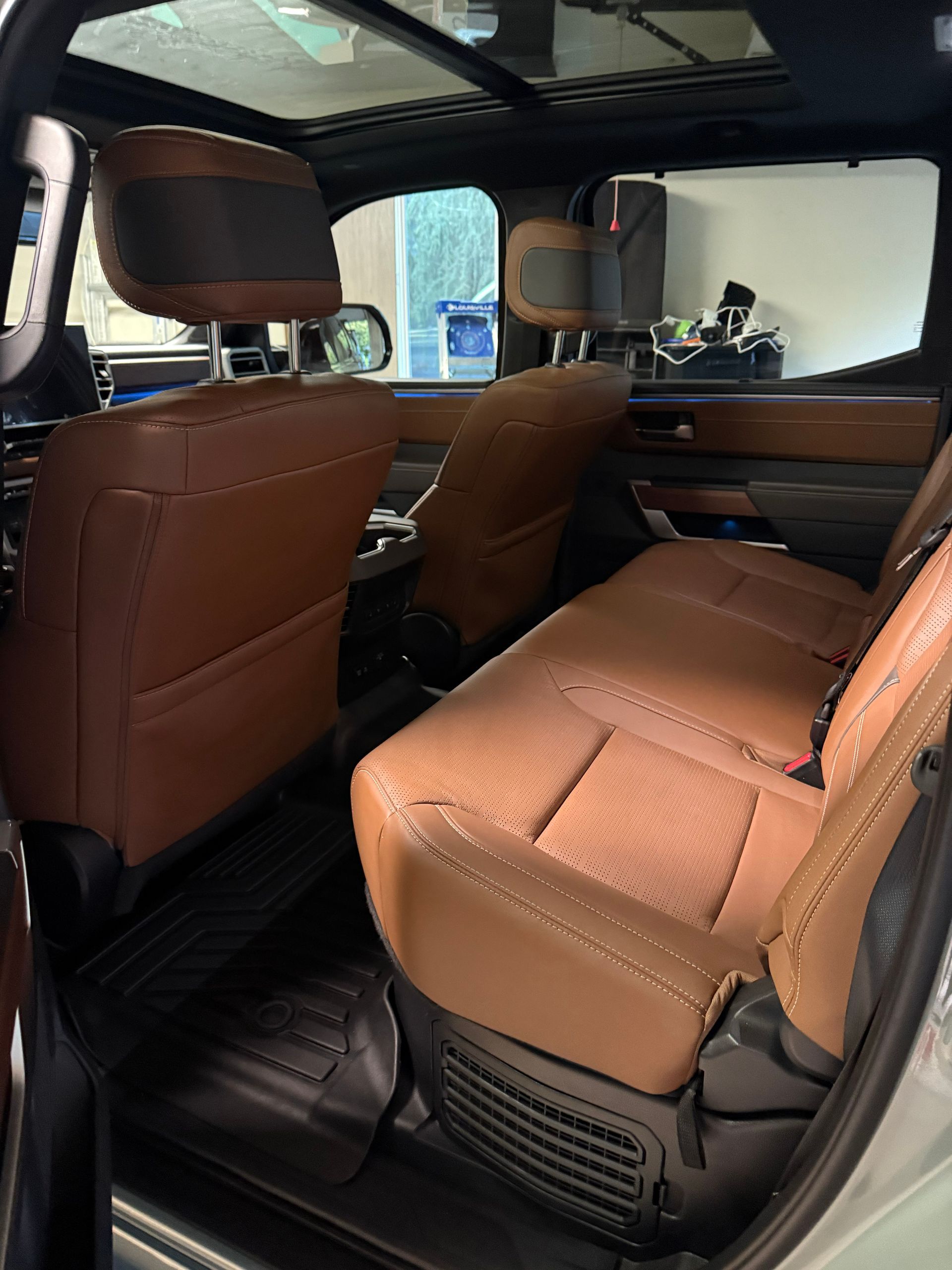 Brown leather car interior with three seats and a rear bench, viewed from the back door