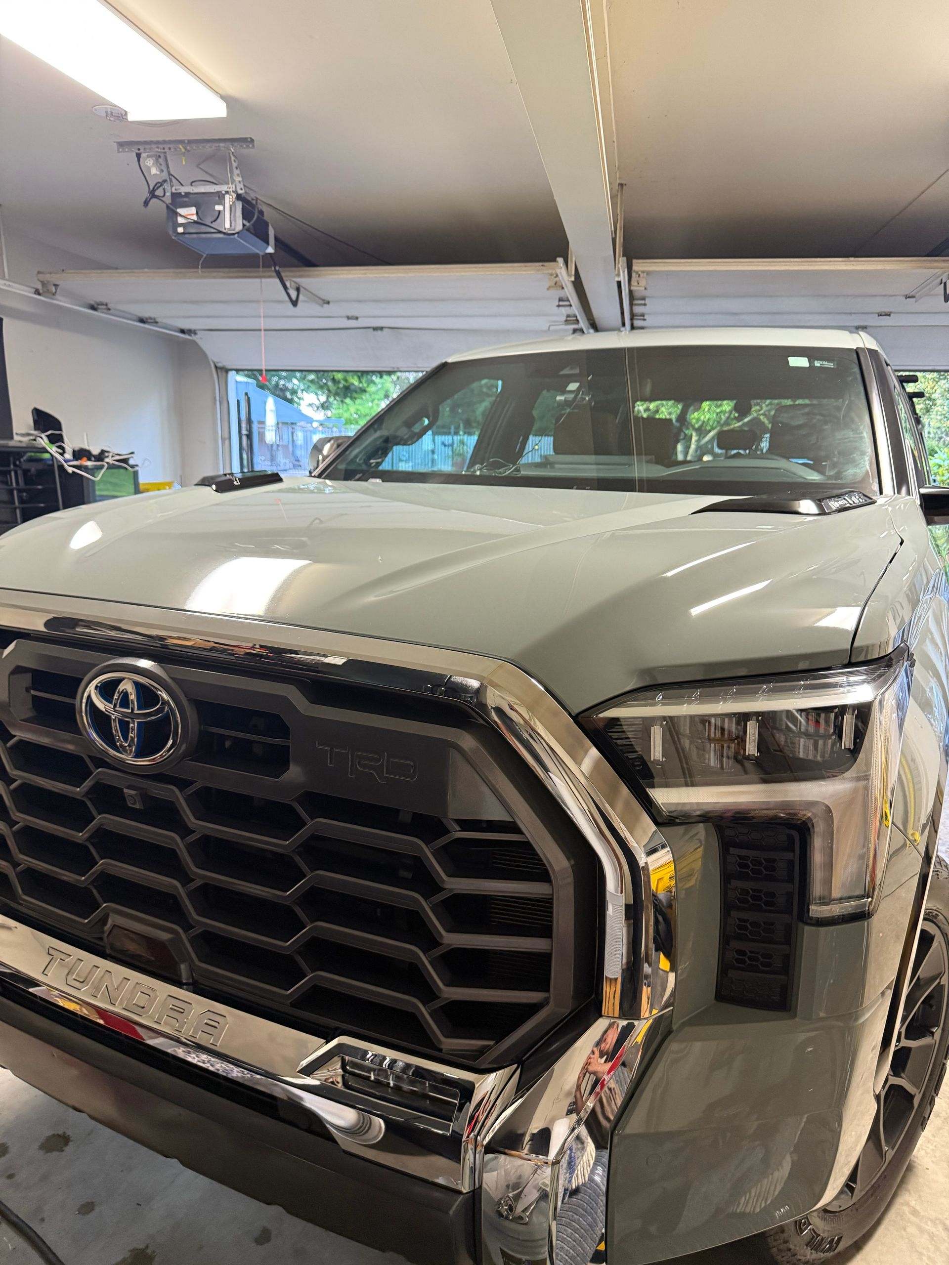 White Toyota truck parked in a garage, with a damaged front grille and bumper.