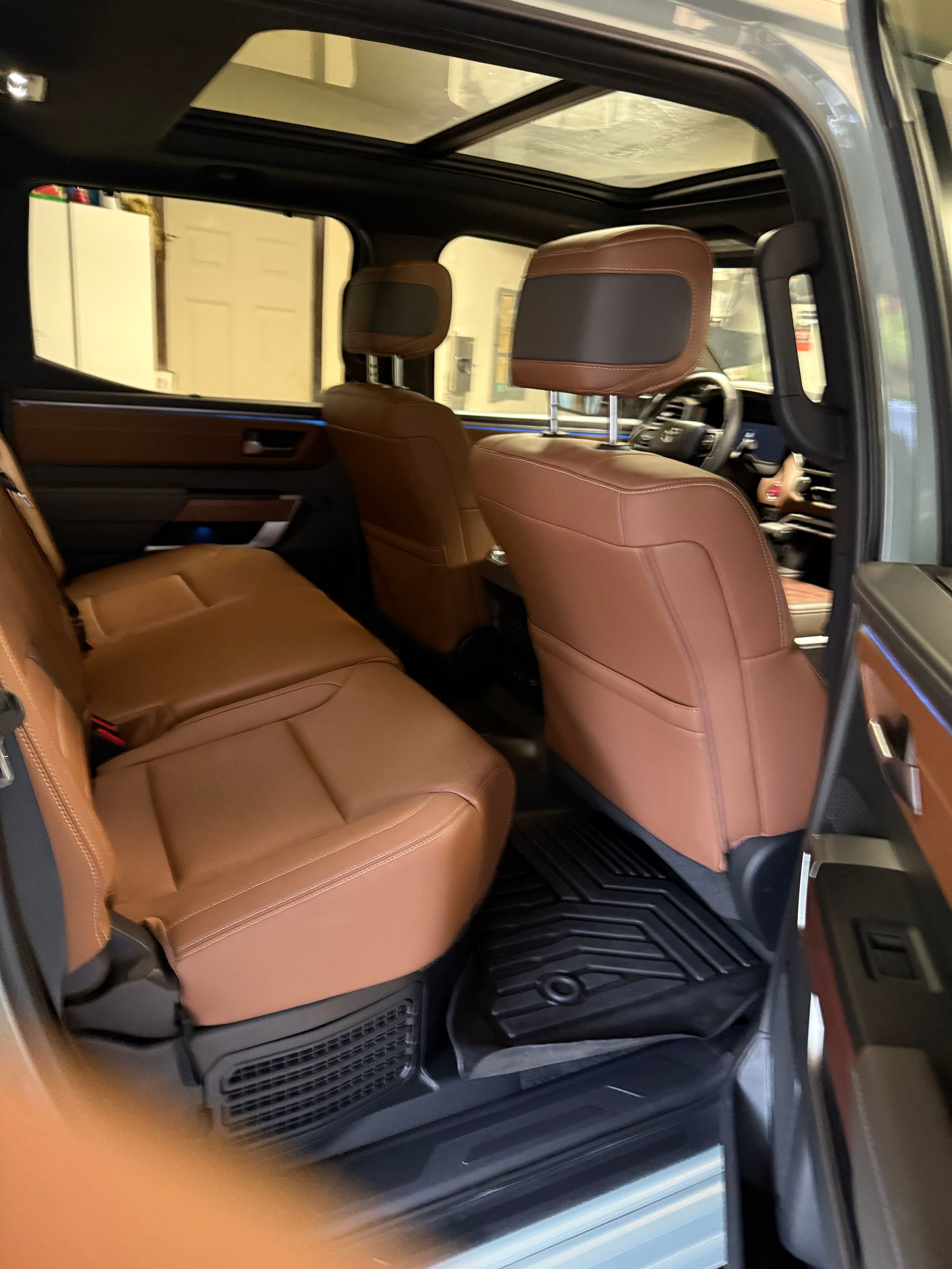 Tan leather SUV rear seats with black floor mats, viewed through the open door.