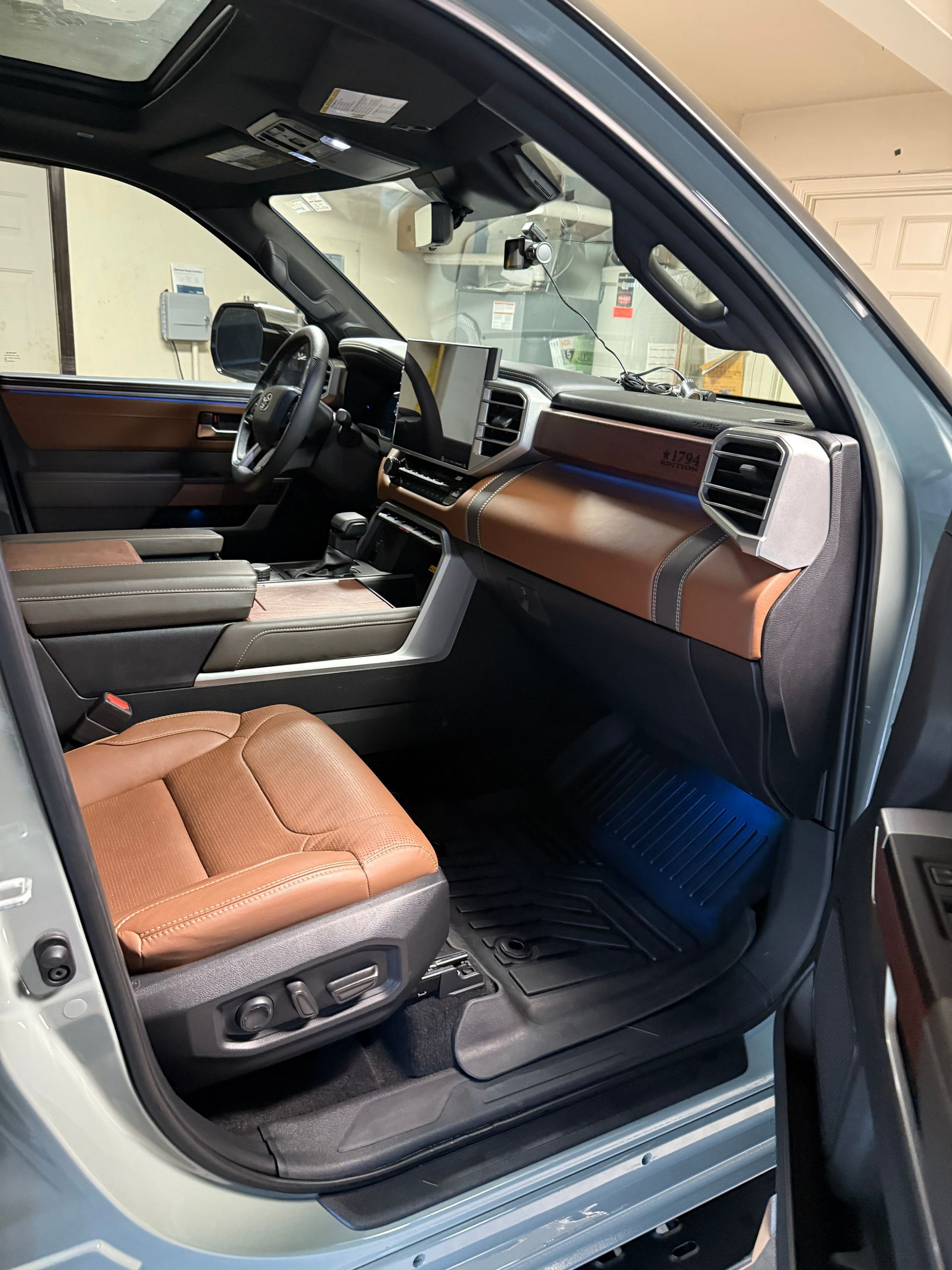 Luxury SUV interior with brown leather seats and dashboard, viewed from the open front door