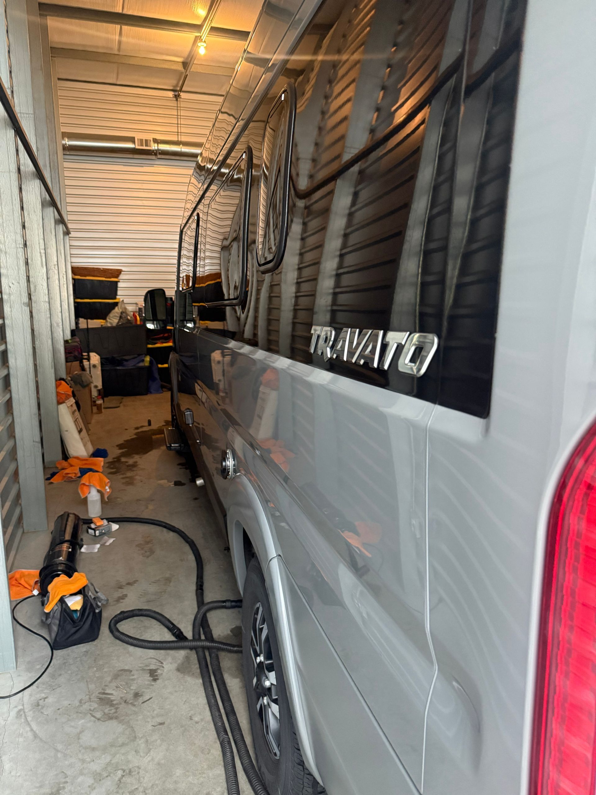 Silver van in a narrow garage, with tools and cables along the side.