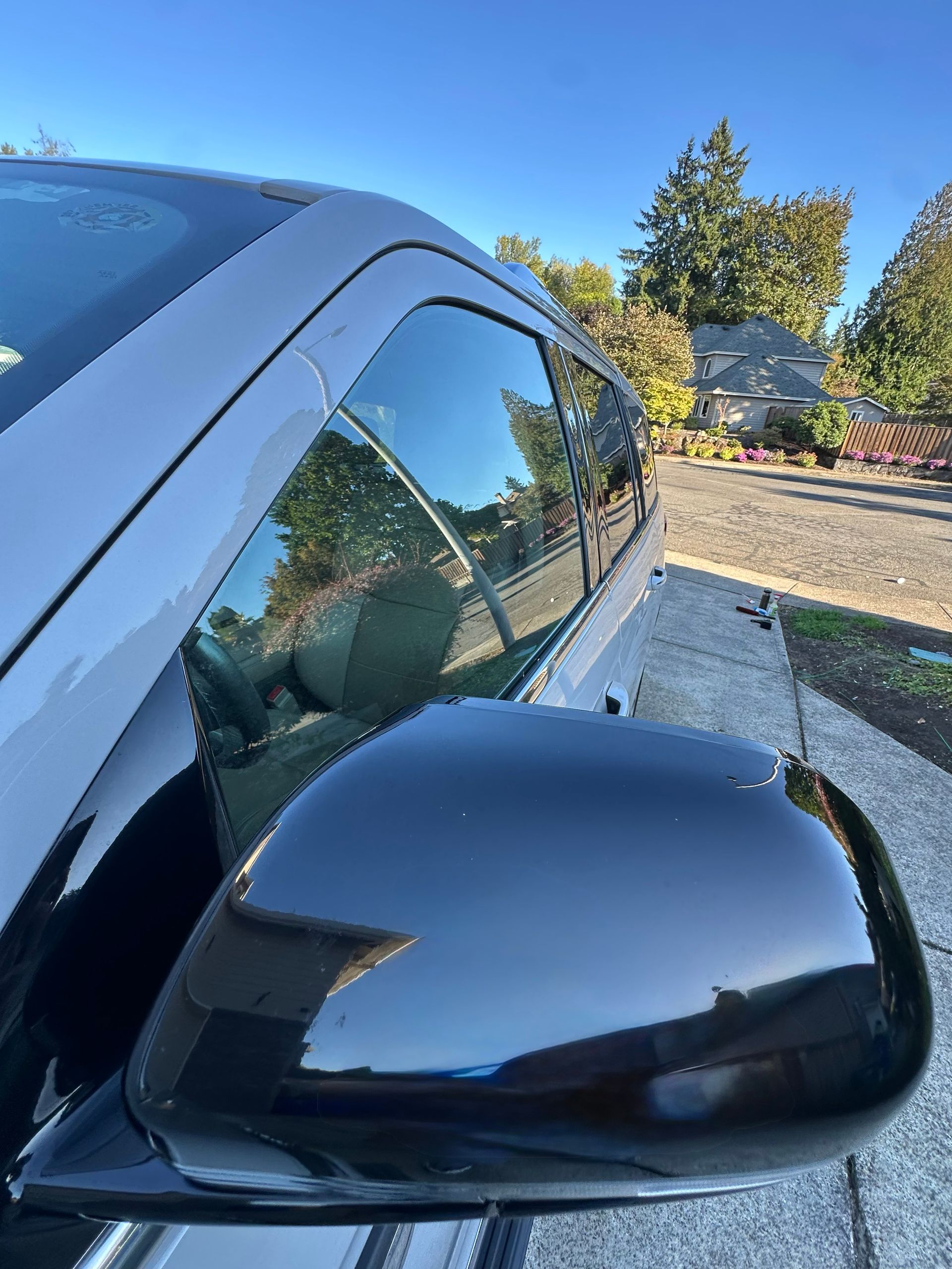 Black car side mirror and window reflecting trees and blue sky on a sunny street