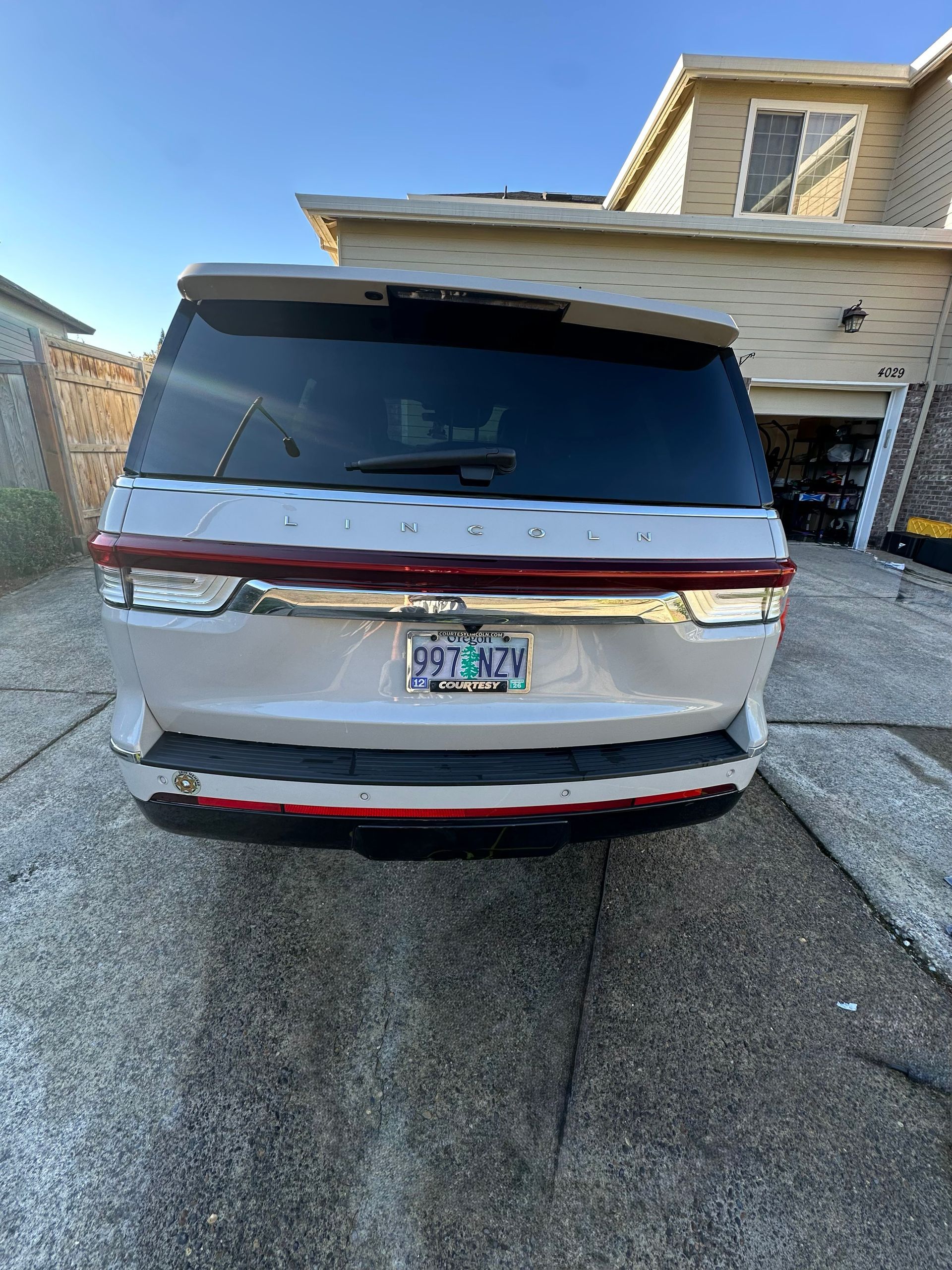 Silver SUV parked in a driveway beside a house, rear view with tinted windows.