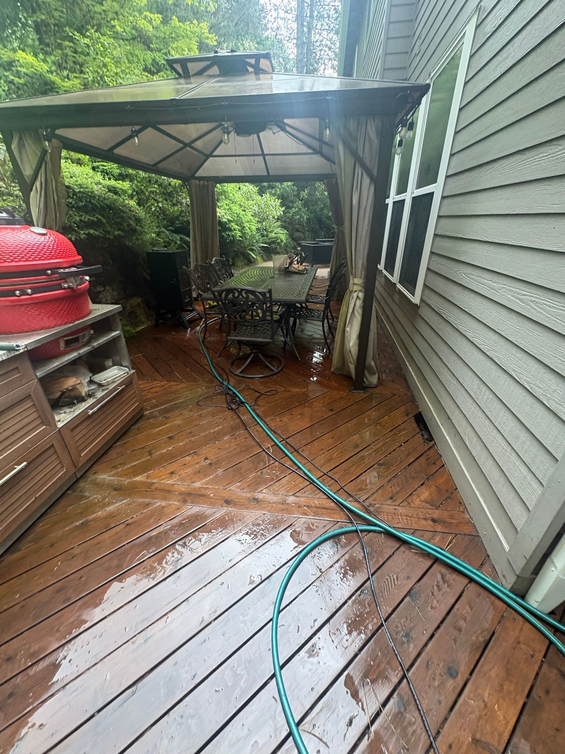 Rainy backyard deck with a hose, canopy, and wet wooden floorboards