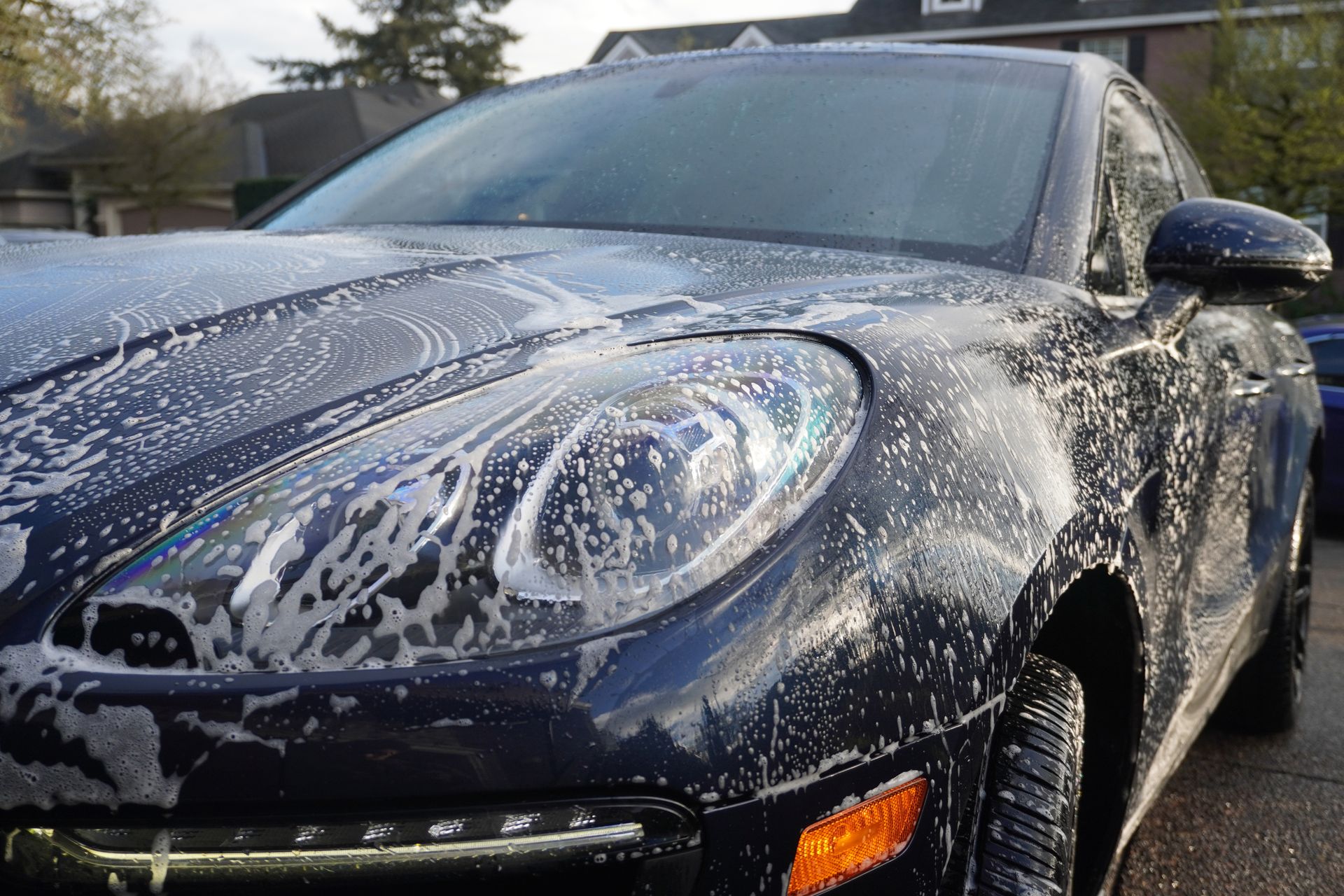 Black car covered in soap suds during a wash, close-up of the front end