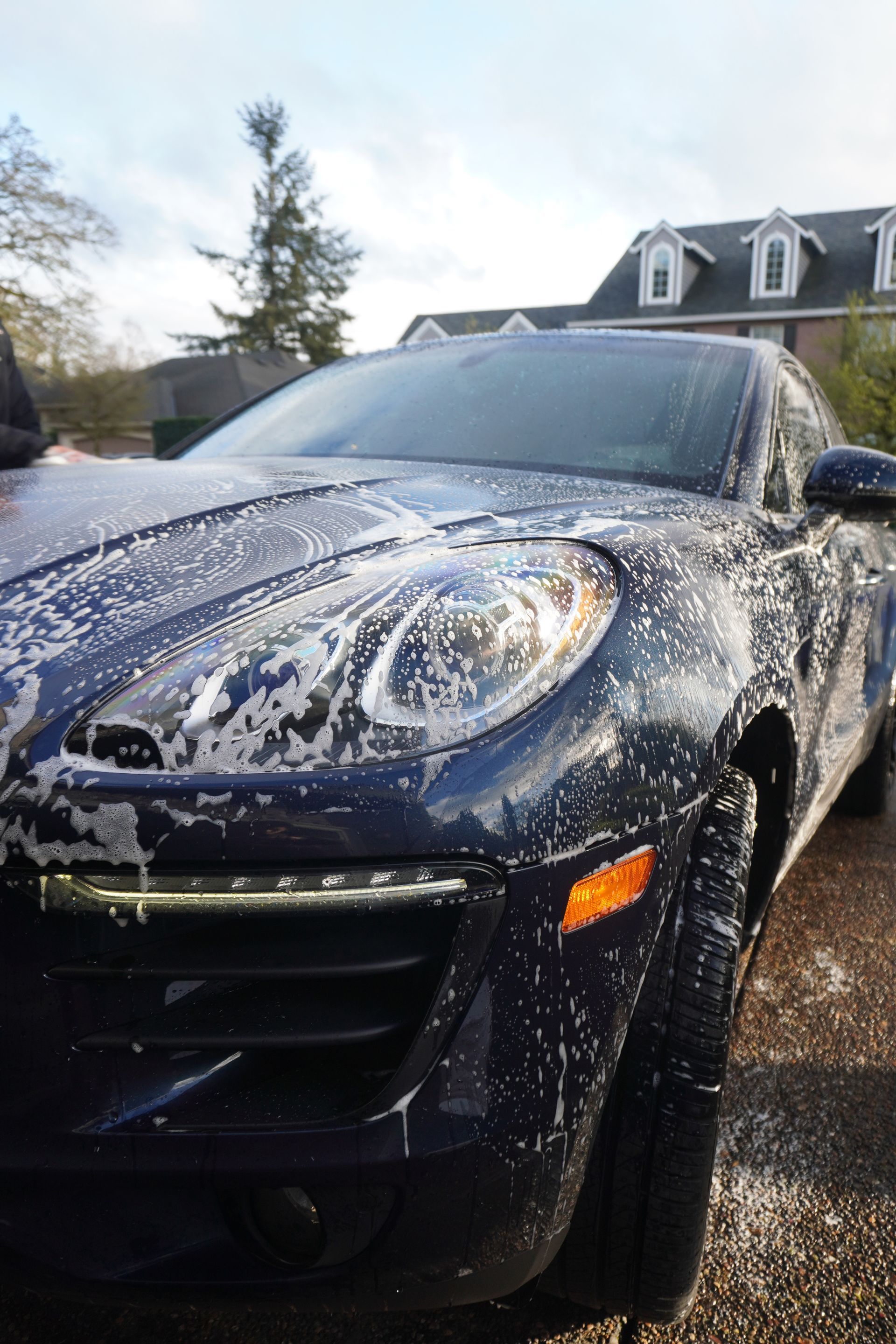 Dark blue car covered in soap suds, parked outdoors in a driveway.