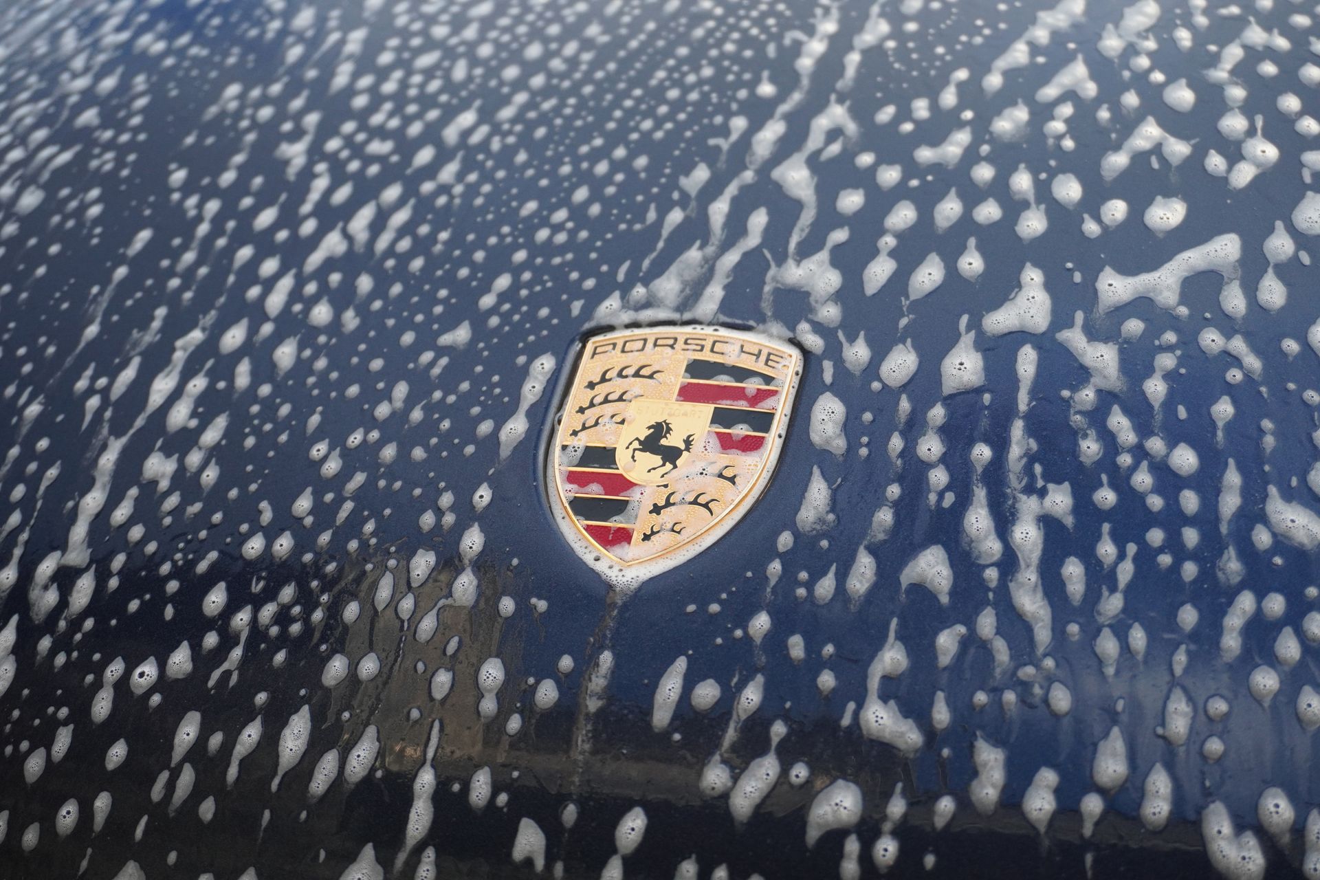 Close-up of a blue Porsche hood covered in water droplets with the Porsche crest centered