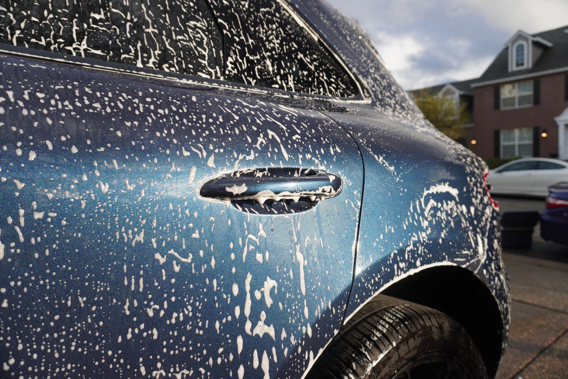 Blue car covered in white soap suds, parked outdoors in a driveway