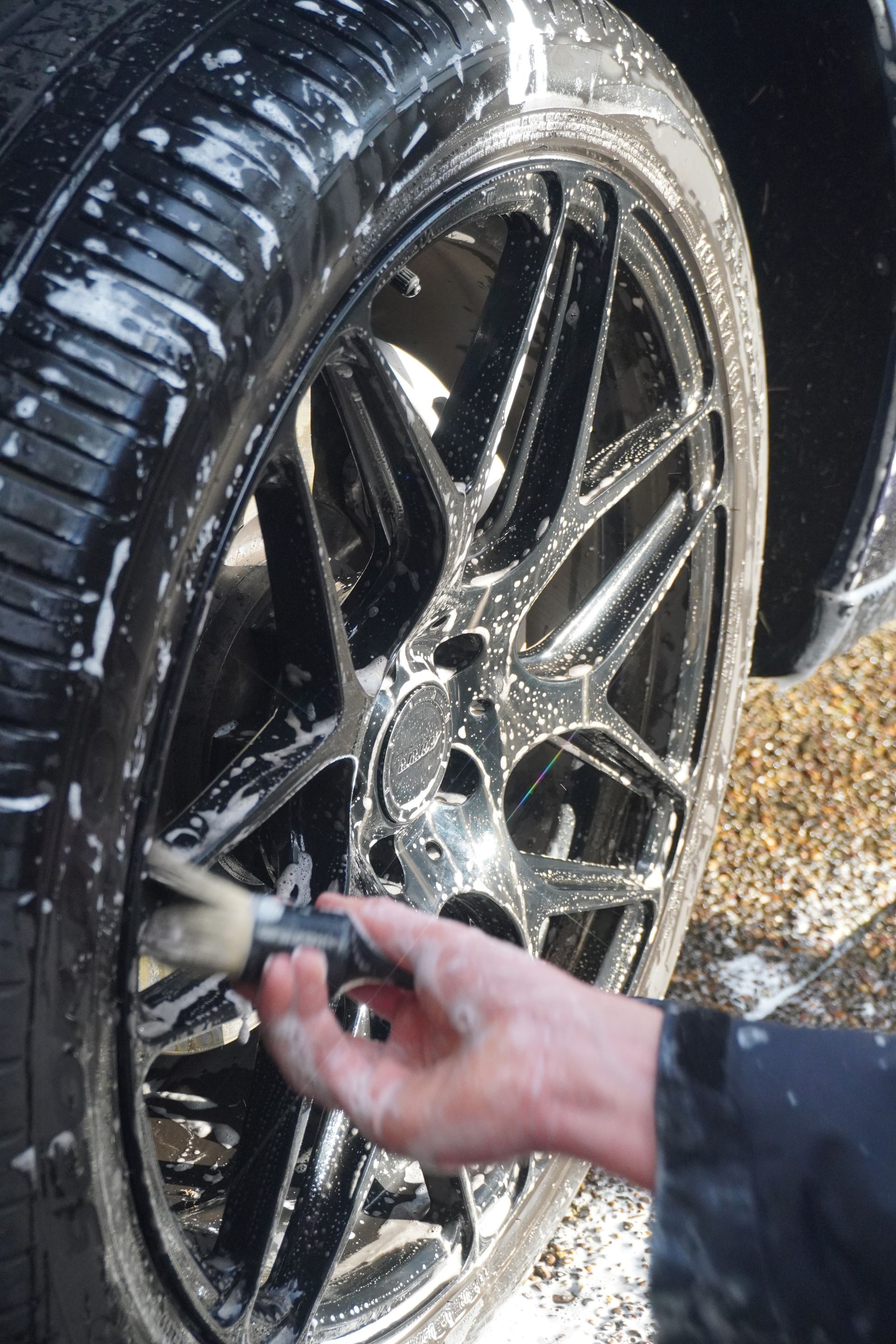 Hand cleaning a wet black alloy car wheel with a brush