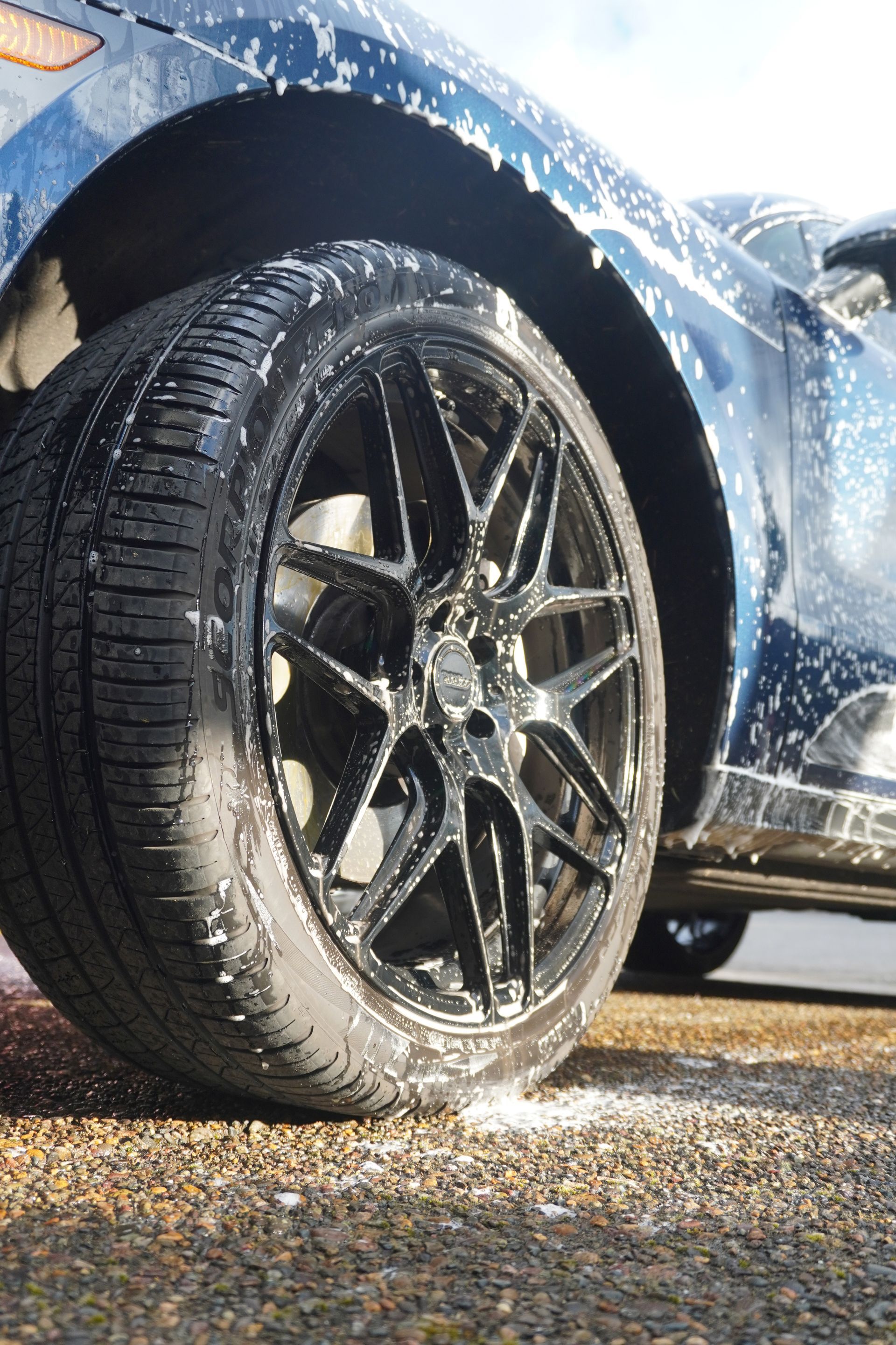 Close-up of a wet black car tire and shiny rim on a blue vehicle in sunlight