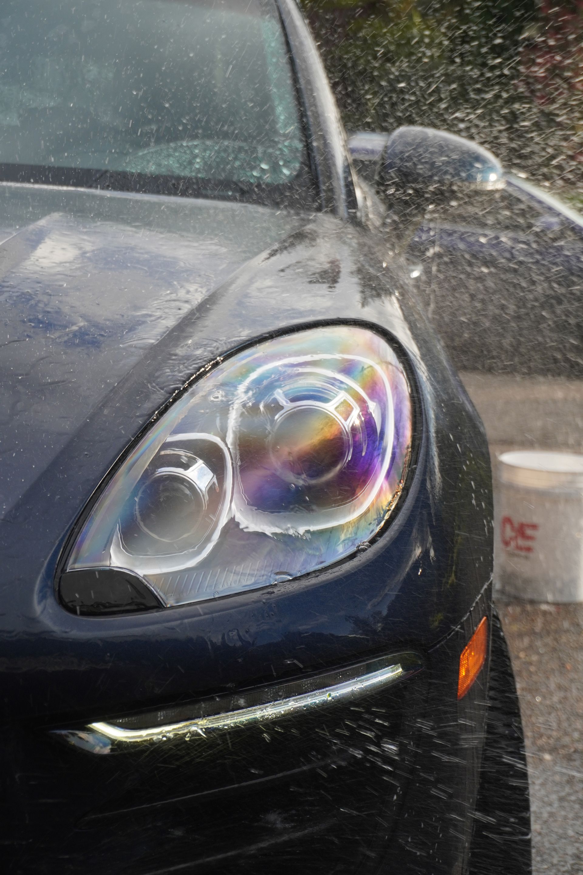 Black car front headlight close-up with raindrops and colorful reflections