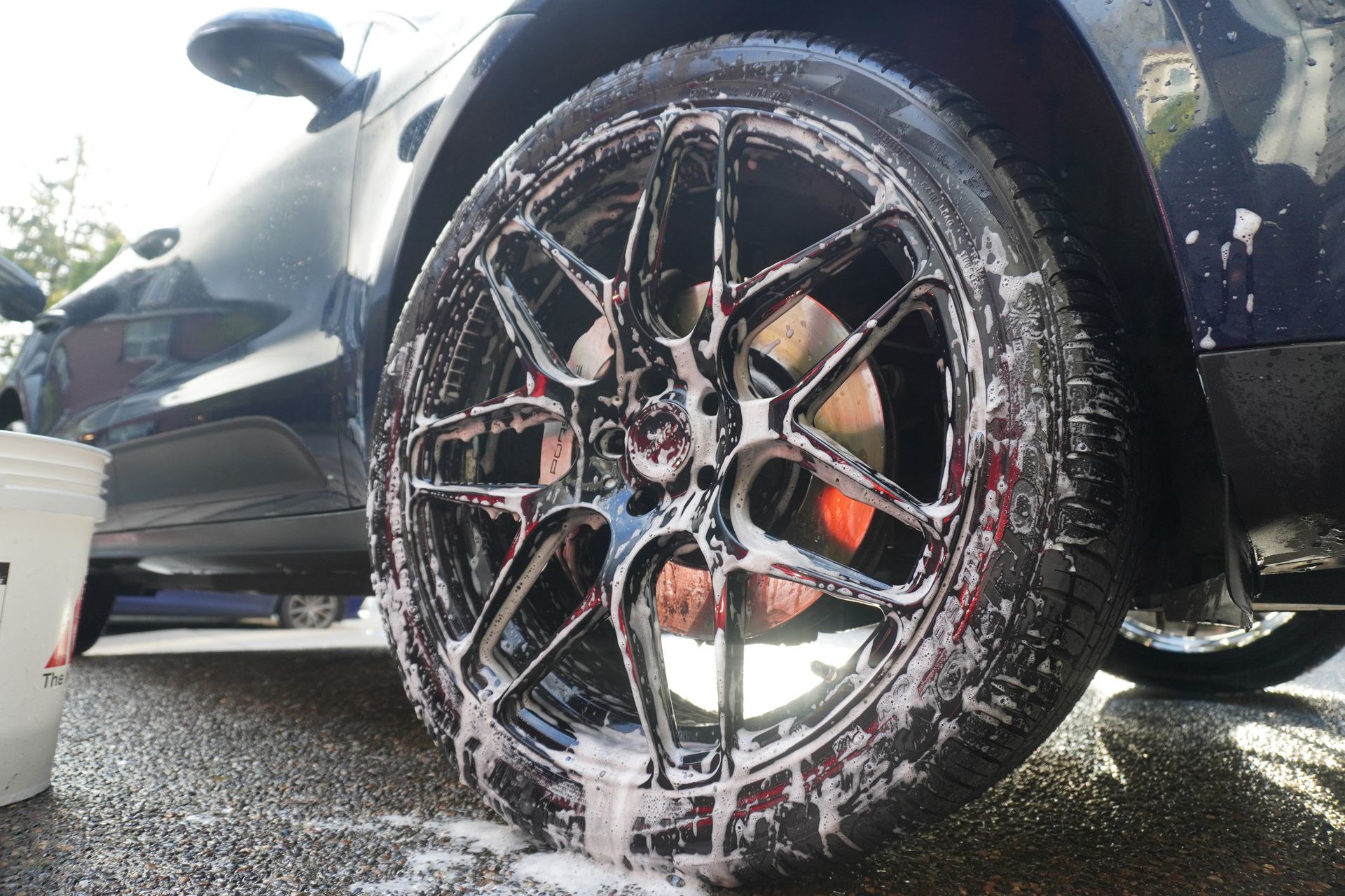 Car wheel being washed with soapy foam at a car wash, close-up of the rim and tire.