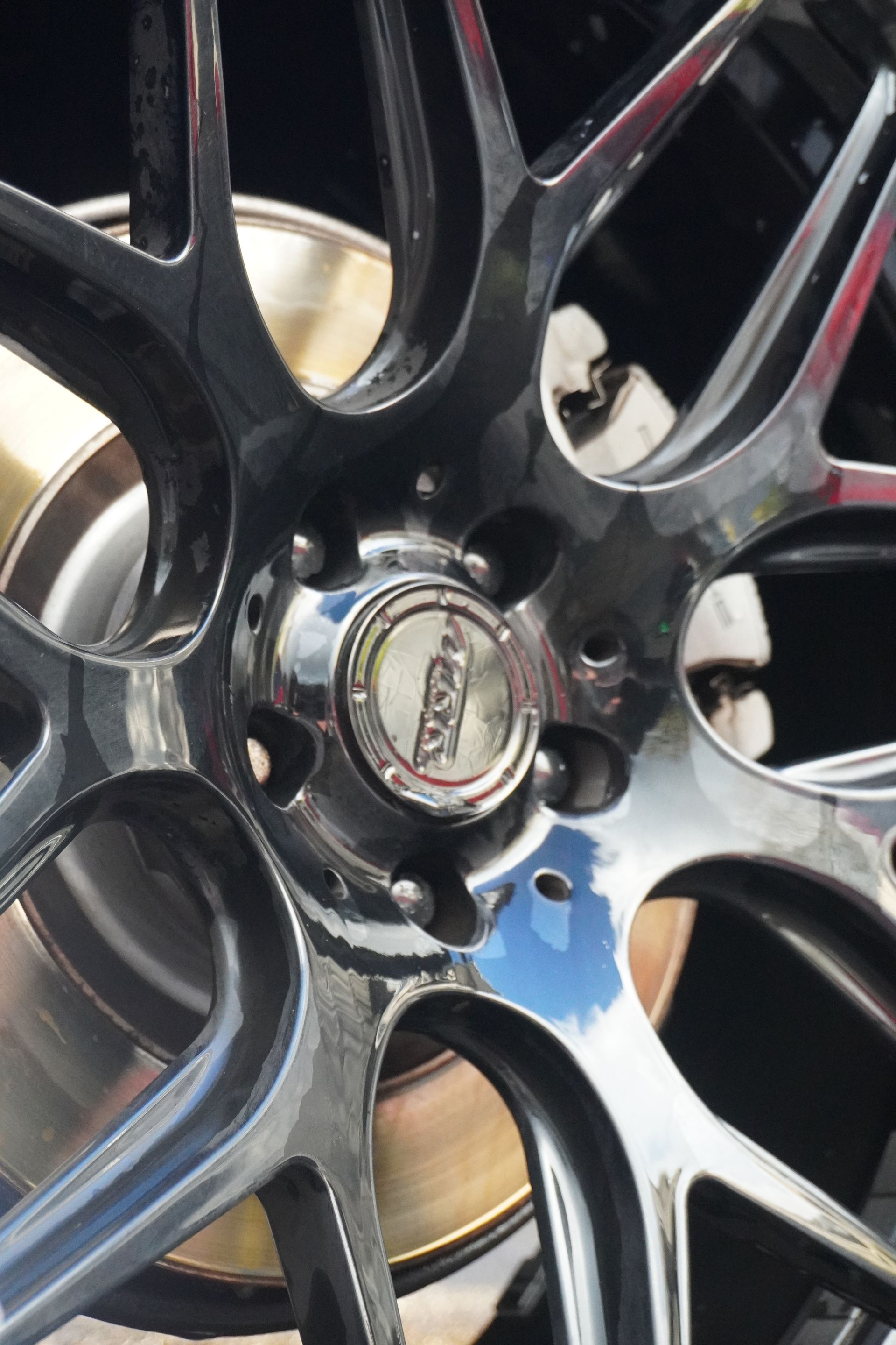 Close-up of a shiny black multi-spoke car wheel rim with a silver center cap.