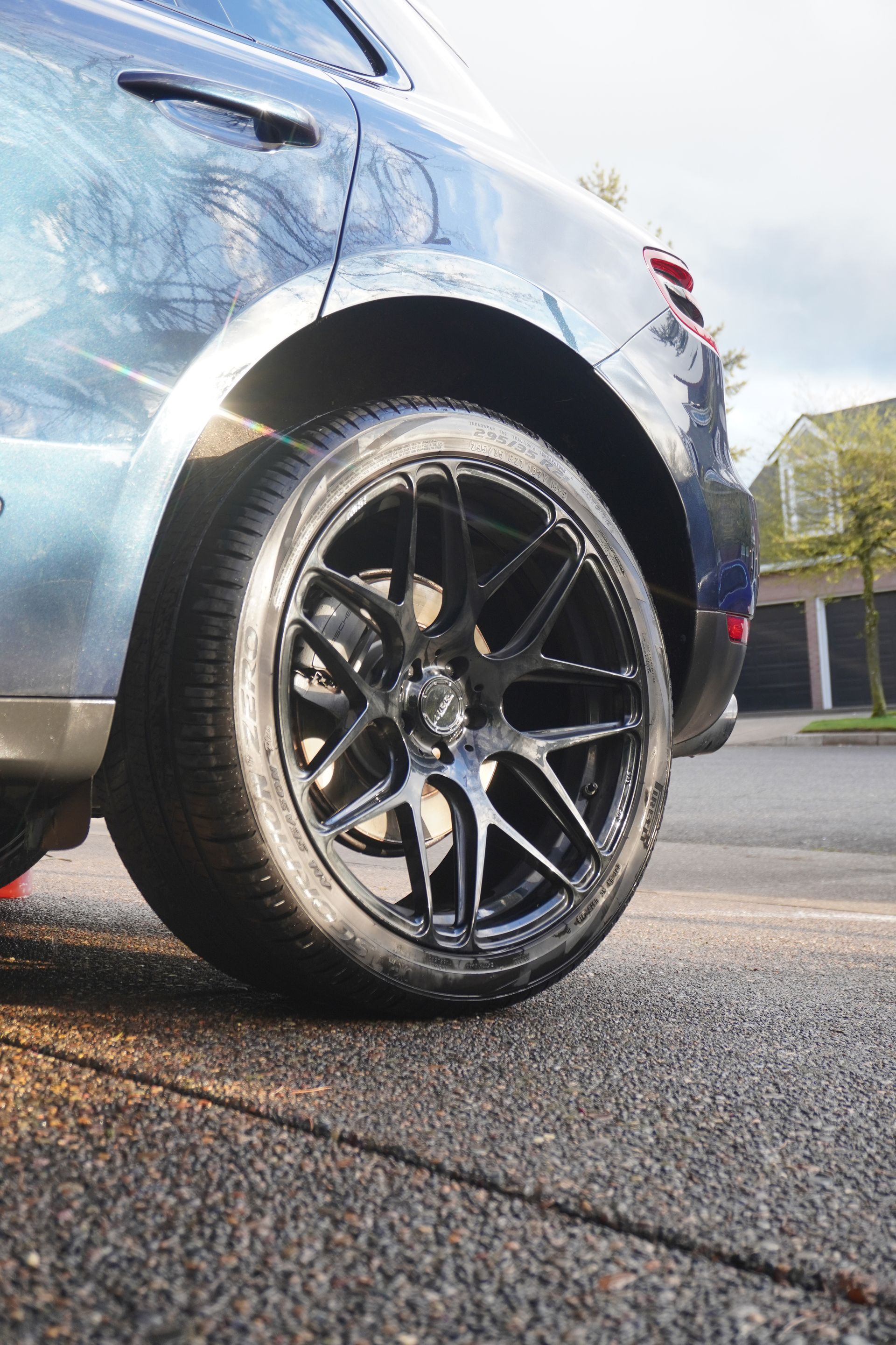 Close-up of a blue car’s black wheel and tire on a wet road, with sunlight reflecting off the body.