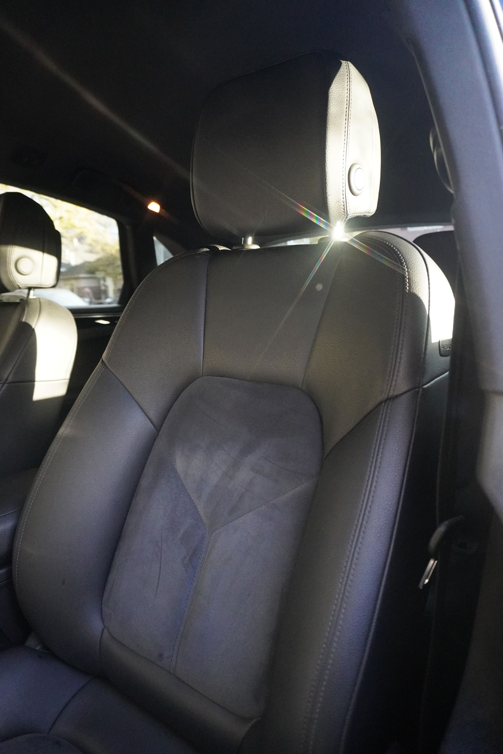 Car interior with a black leather front seat and headrest, lit by sunlight.