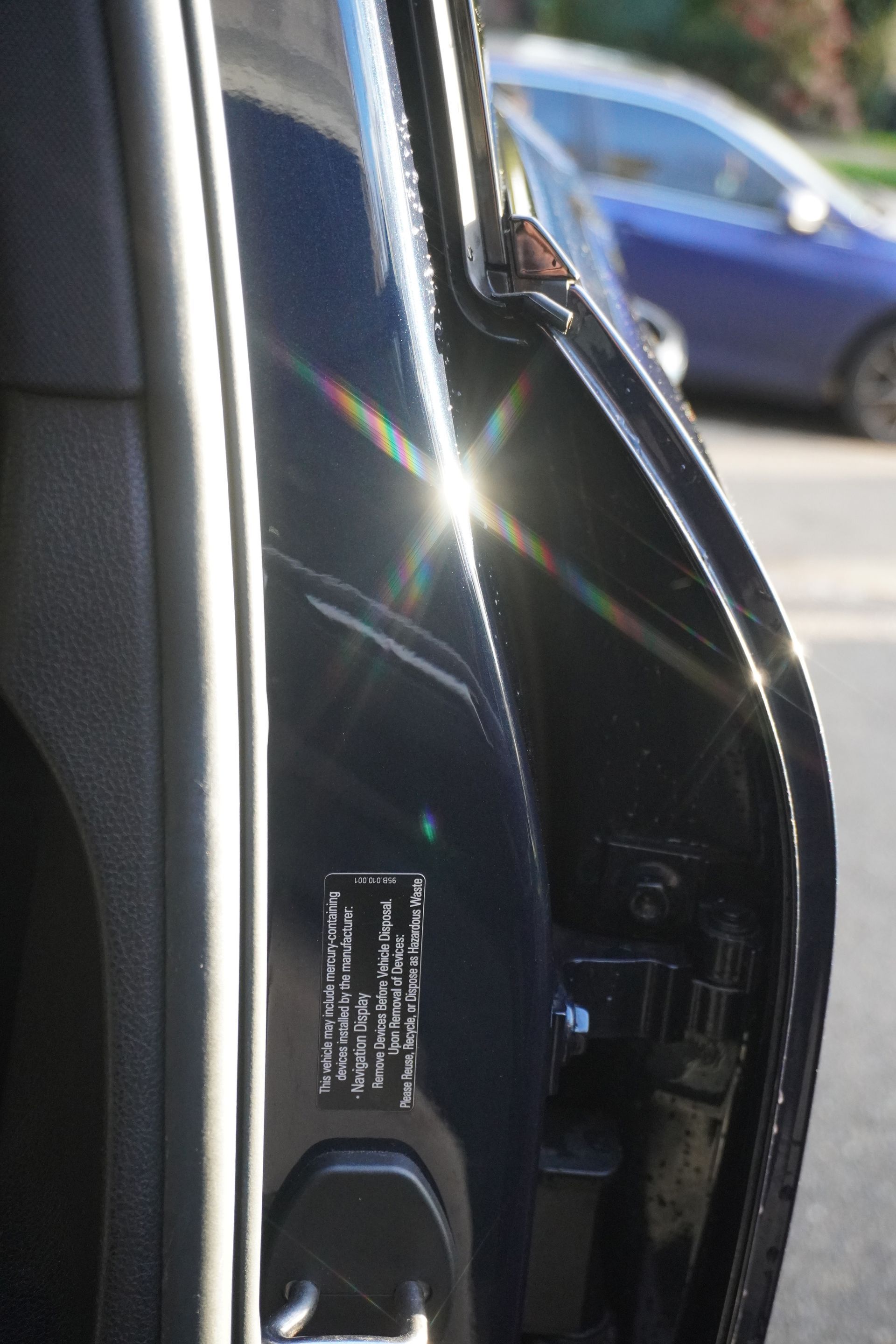 Close-up of a black car door edge with sunlight glare, showing the door latch area.