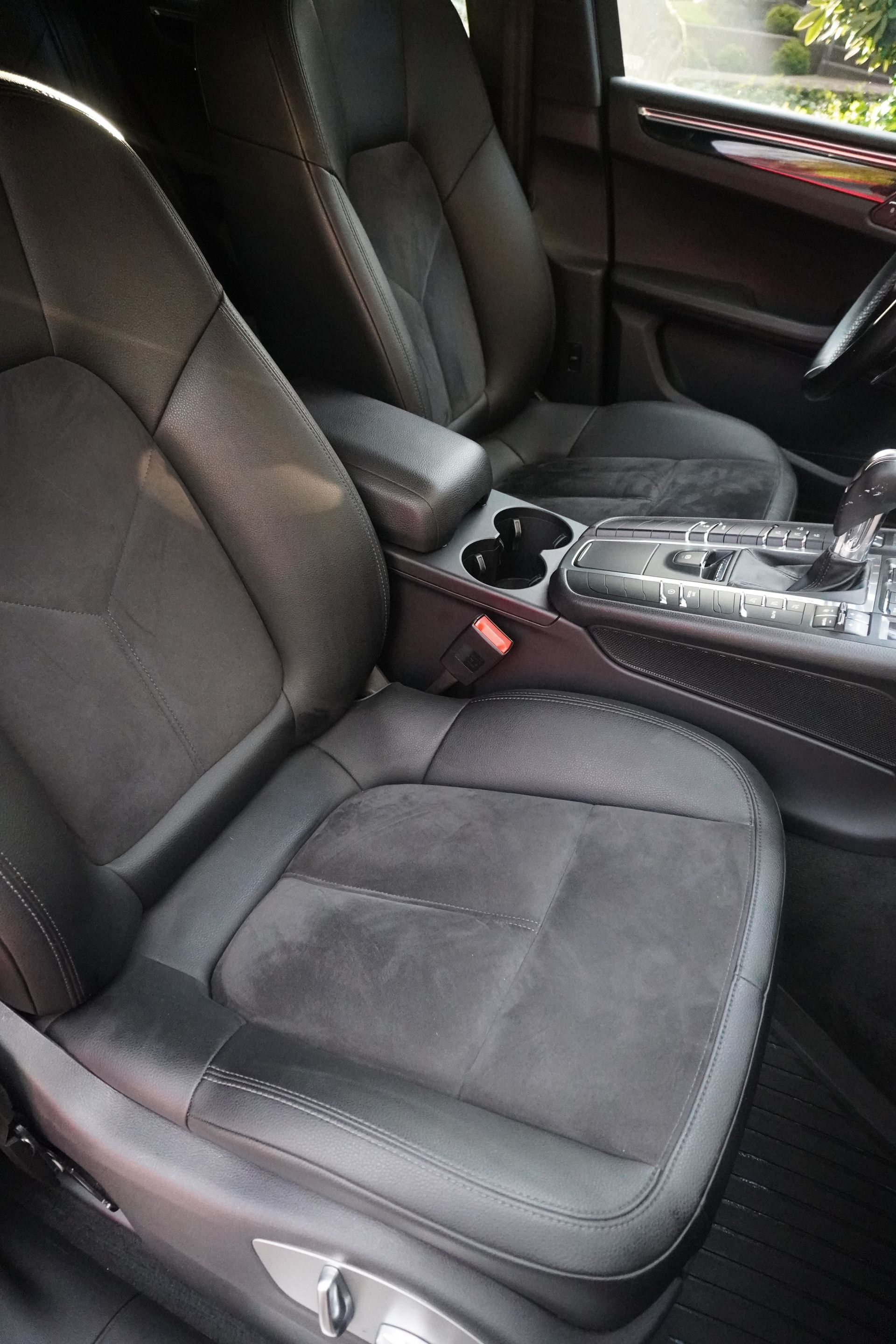 Front passenger car seat and center console with cup holders and gear shifter, black leather interior.