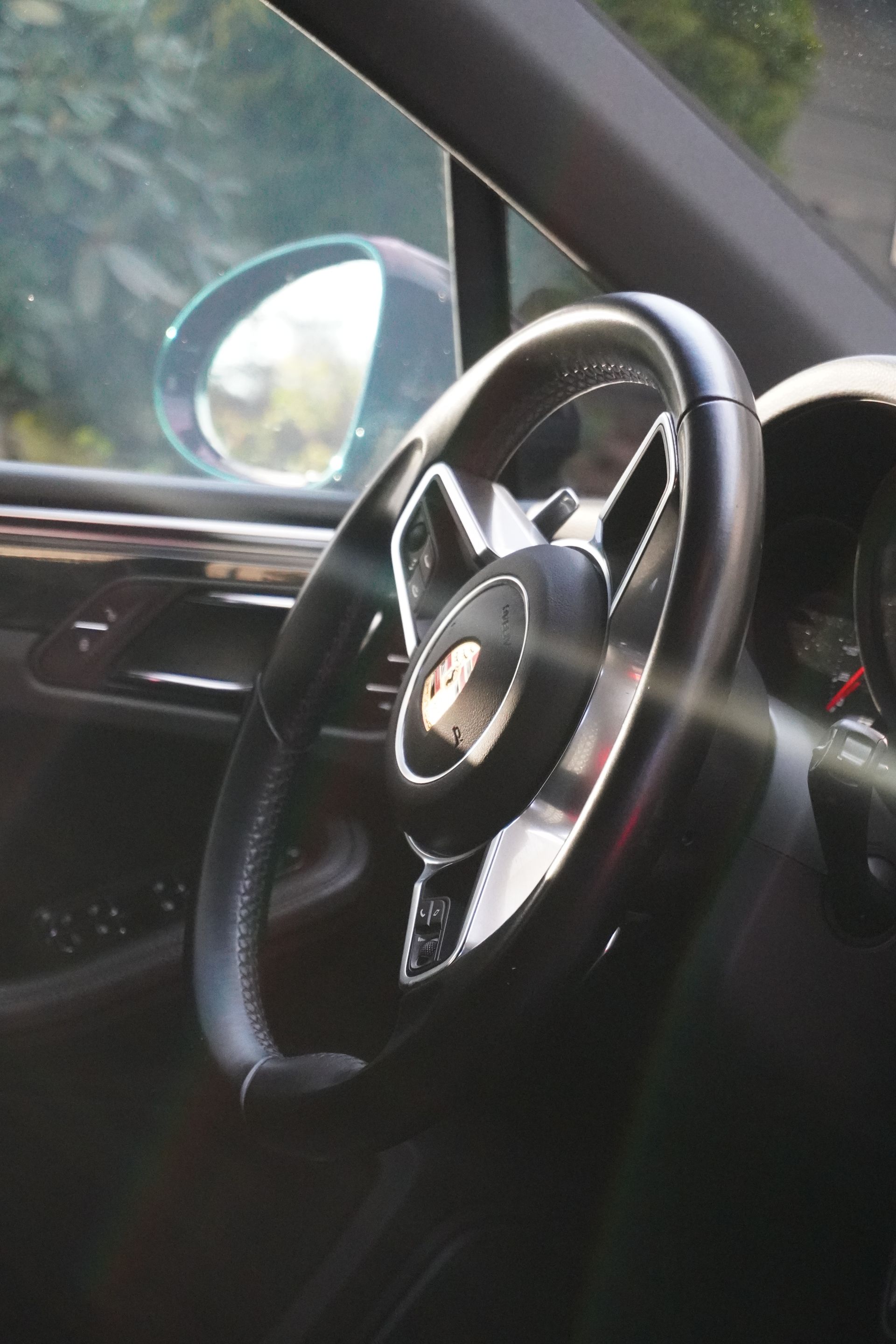 Car interior with a black steering wheel, driver’s door panel, and side mirror visible.