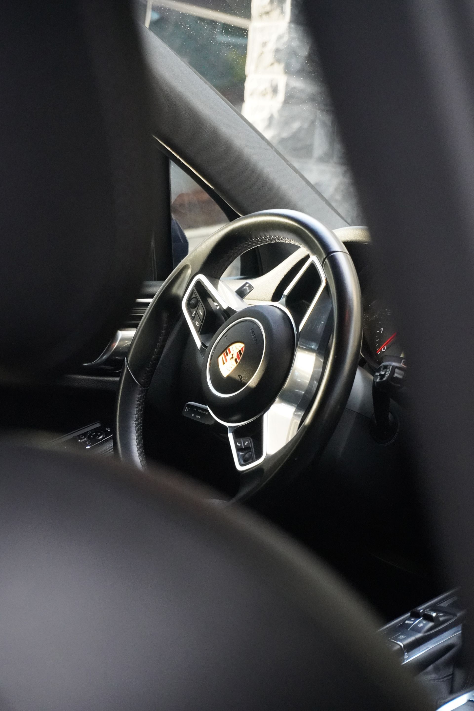 Porsche steering wheel and dashboard seen through a car interior window
