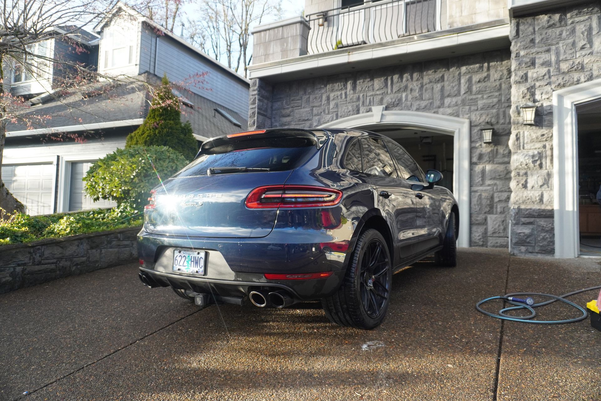 Blue SUV parked in a driveway beside a stone house, with water spraying on the pavement.