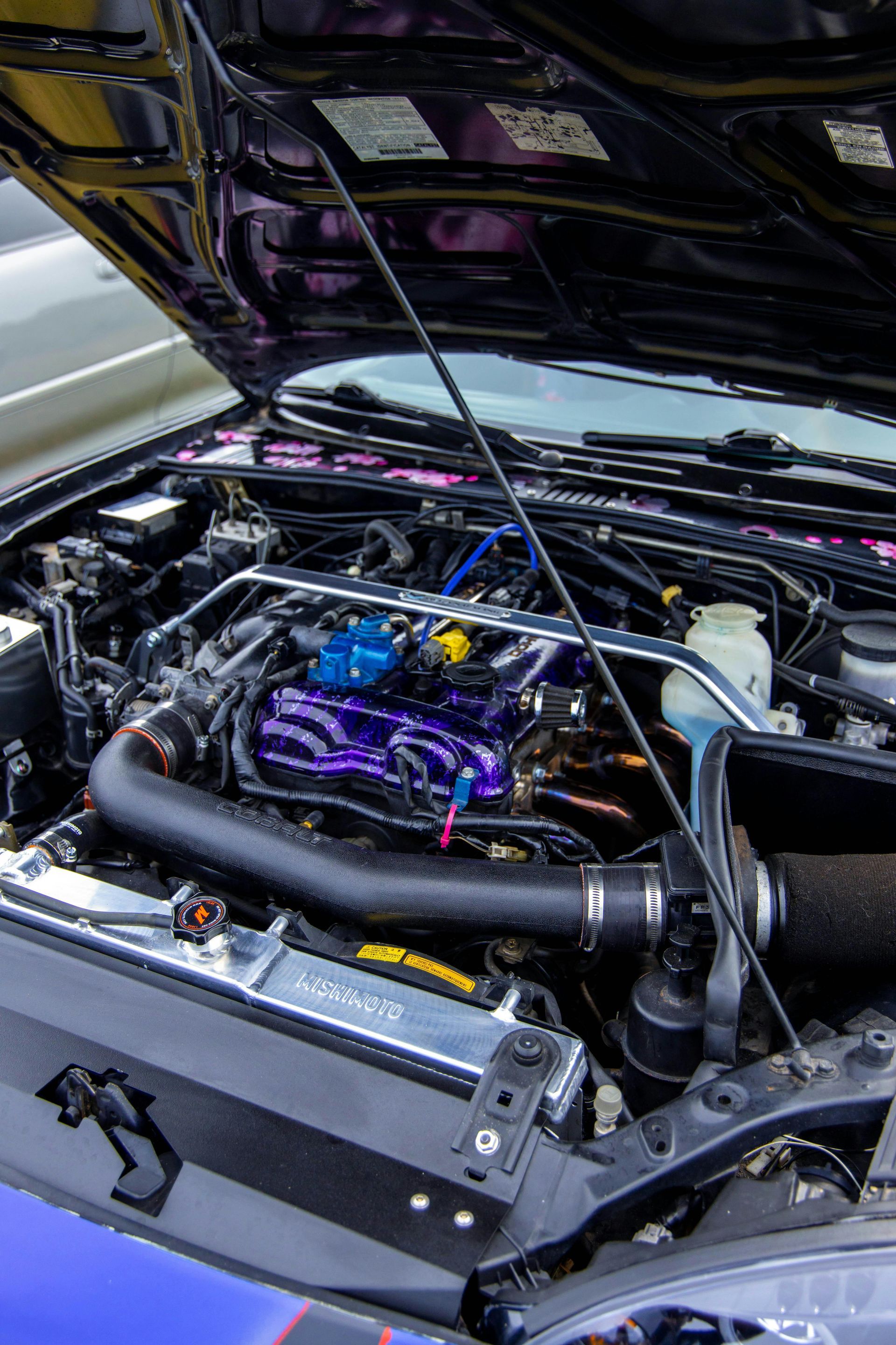 Open car engine bay with purple components and a large intake hose, hood raised.