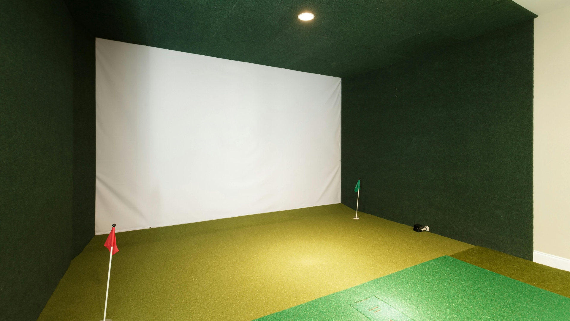 Indoor room with green turf flooring, black cubicle-like structures, and white partition walls under exposed ceiling beams