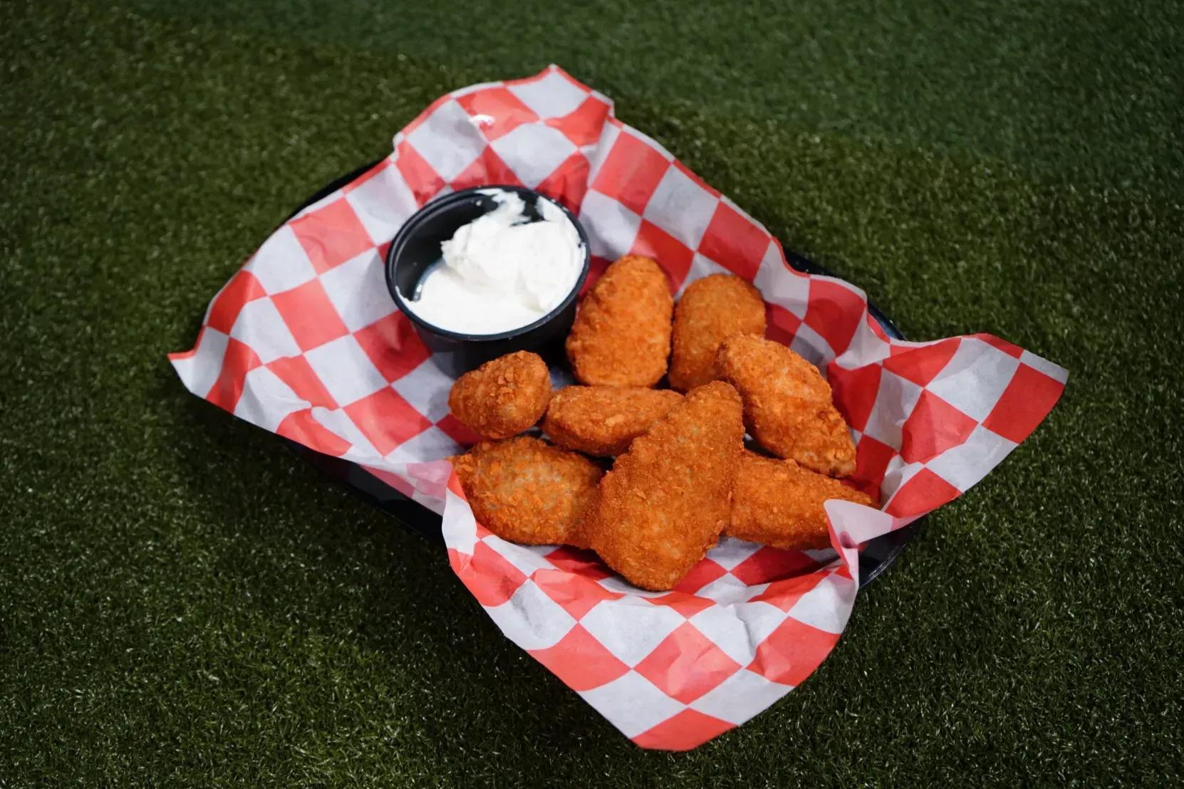 Chicken nuggets with dipping sauce in a red-and-white checkered basket on grass