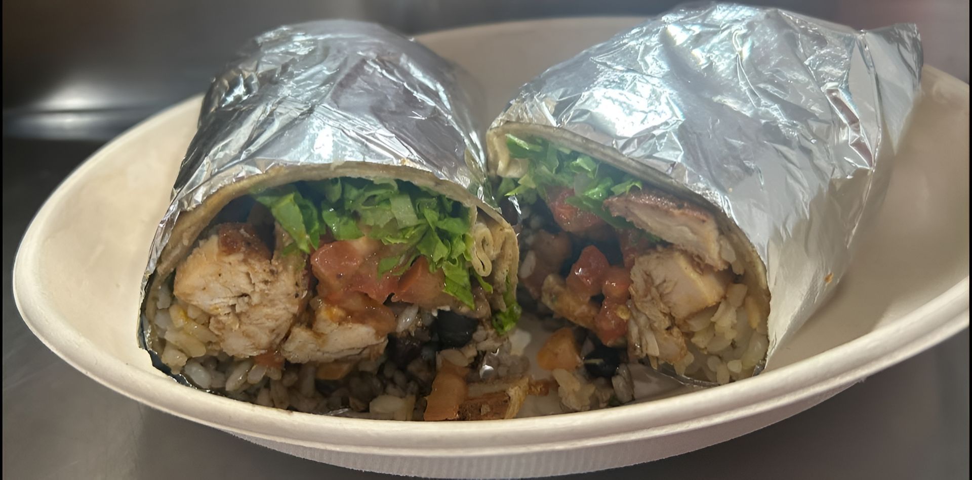 Two halves of a chicken burrito in foil, in a white bowl.