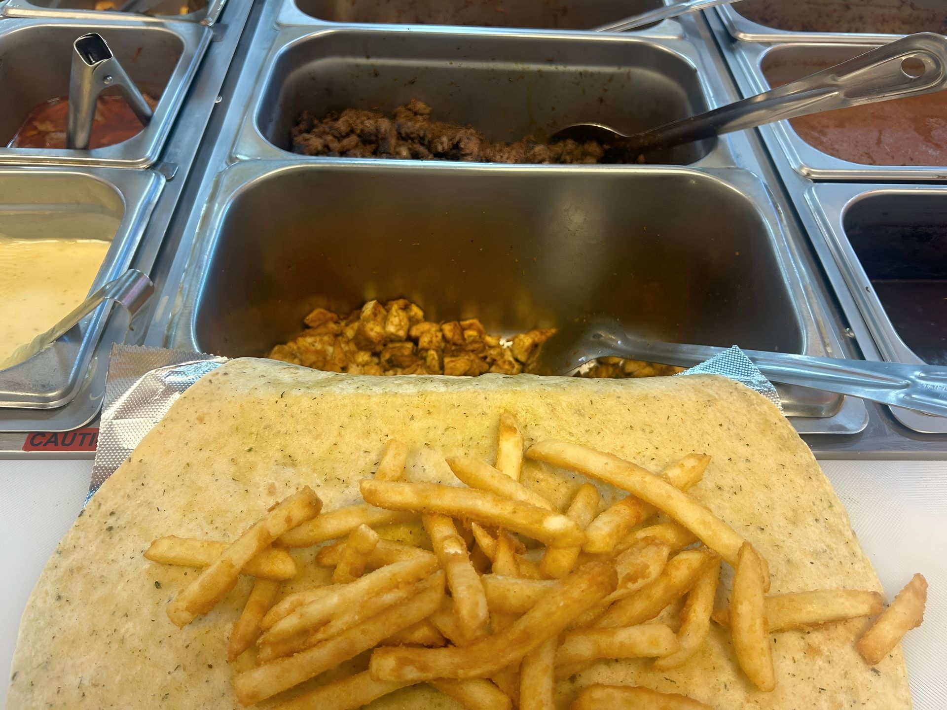 A tortilla with fries, awaiting fillings from food trays above.