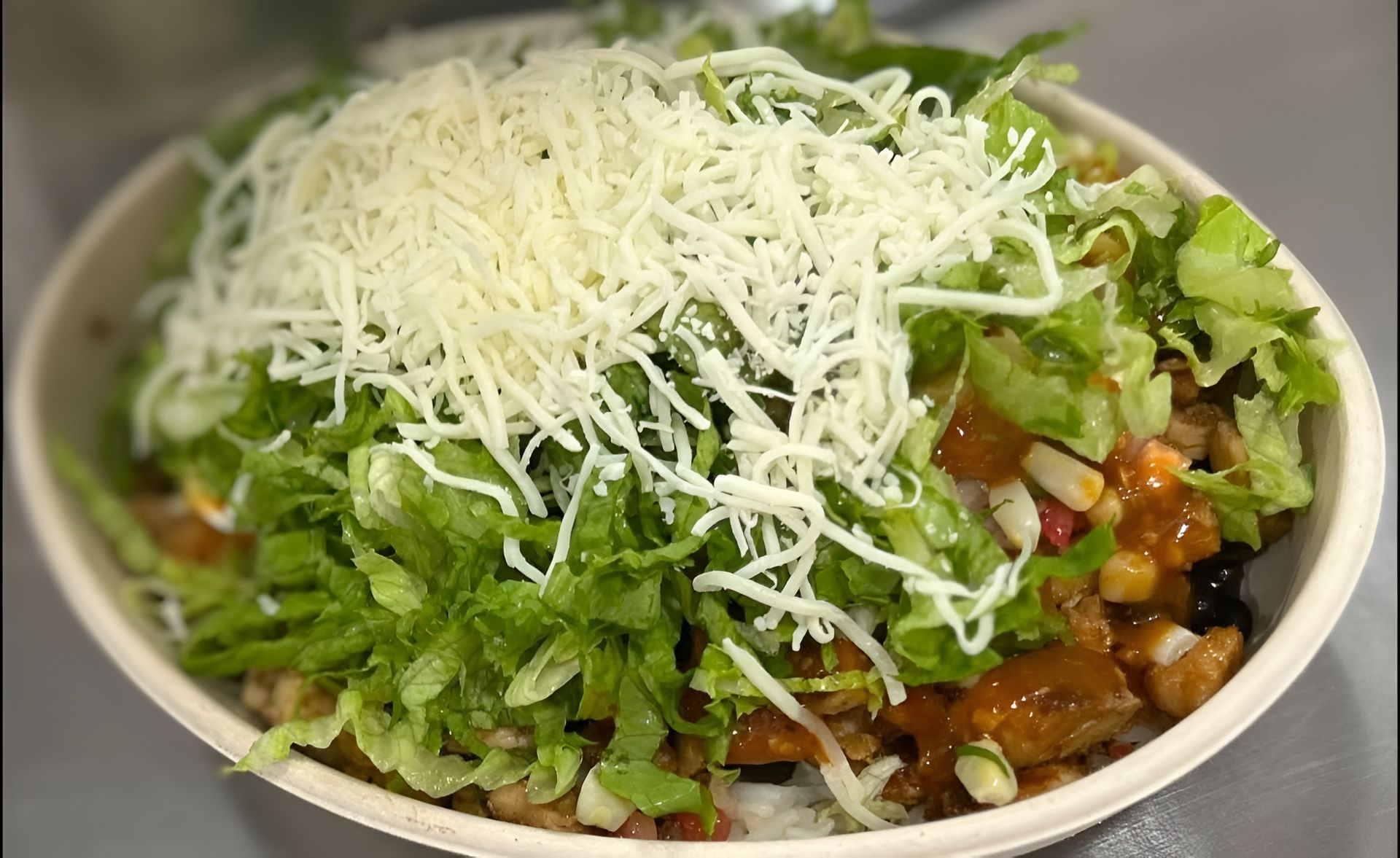 Bowl of food with shredded cheese, lettuce, and sauce.